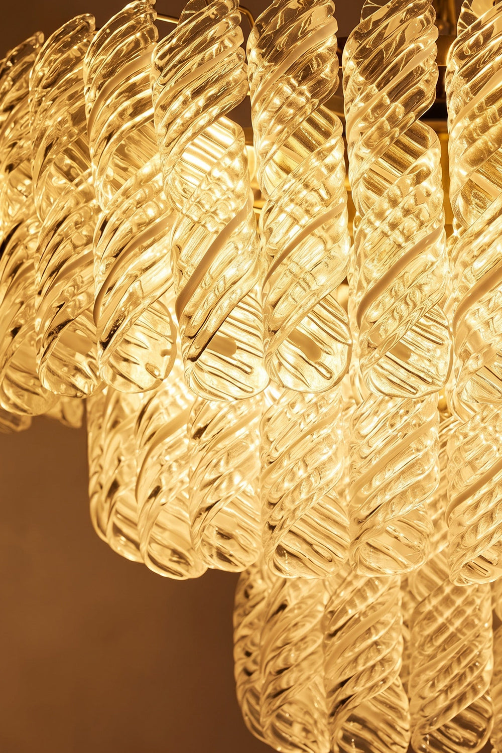Evangeline Tiered Twisted Glass Chandelier | Illuminated Glass Detail | Close-up macro view of the fully lit clear twisted glass cylinders showcasing the warm golden light refraction | Detail shot | Samu Lamp