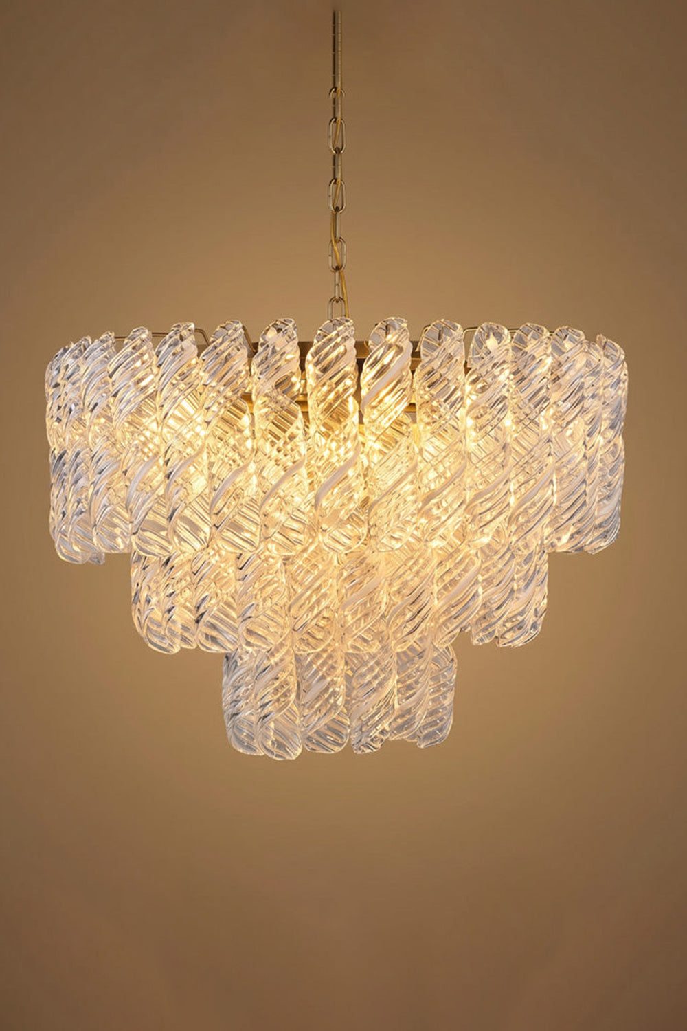 Evangeline Tiered Twisted Glass Chandelier | Studio Lit Presentation | Fully lit tiered luxury glass chandelier casting a deep warm golden halo against a neutral beige background | Samu Lamp