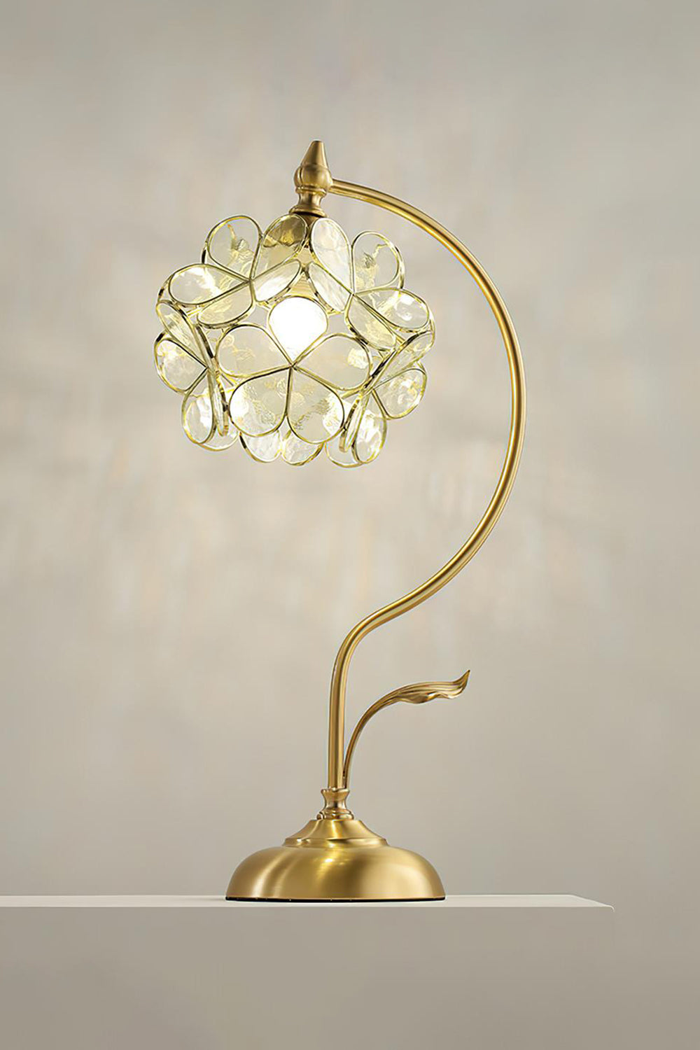 Evanthe Blossom Stained Glass Table Lamp | Stained Glass, Metal | Fully illuminated warm cream white variant casting a brilliant textured shadow halo on a grey studio wall | Samu Lamp