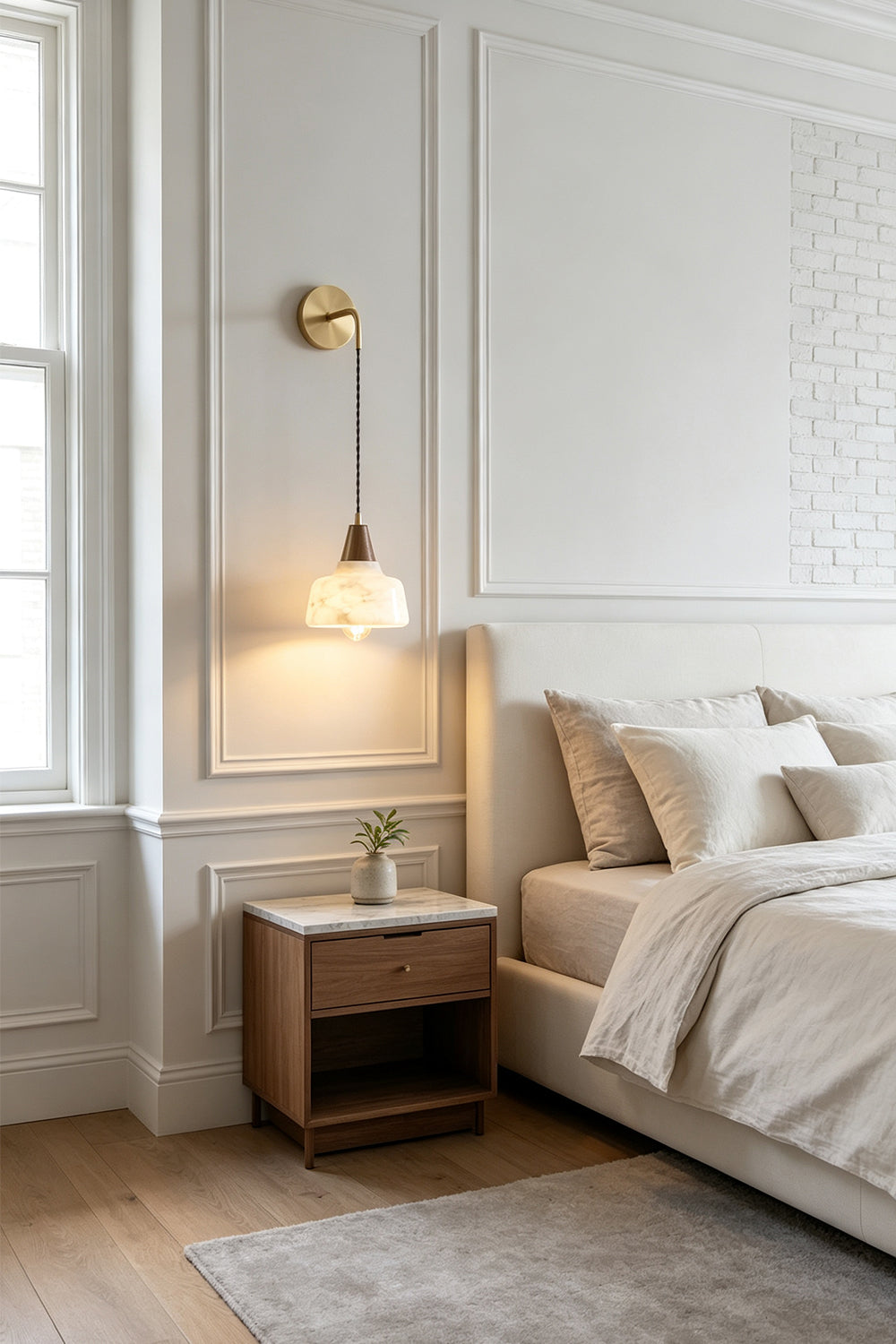Everett Alabaster Hook-Arm Wall Sconce illuminating a bedside with a modern design and natural accents.
