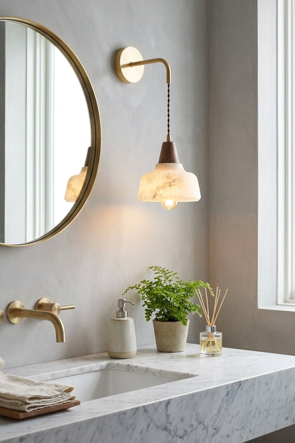 Everett Alabaster Hook-Arm Wall Sconce in a modern bathroom setting with a mirror and plants.