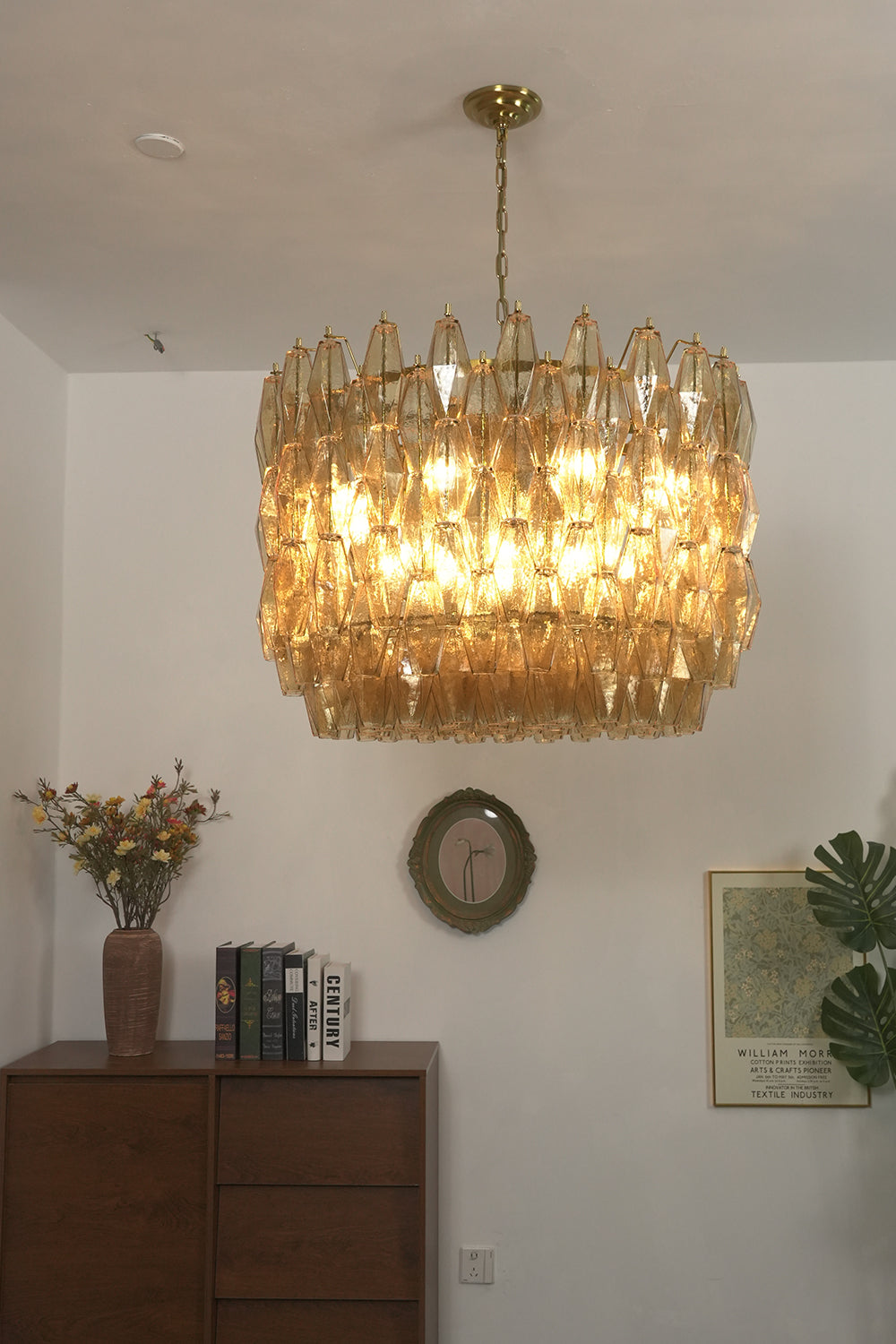 Lit amber drum Sorrento chandelier | Metal, Glass | Mounted above a dark wooden cabinet in a living room | Samu Lamp