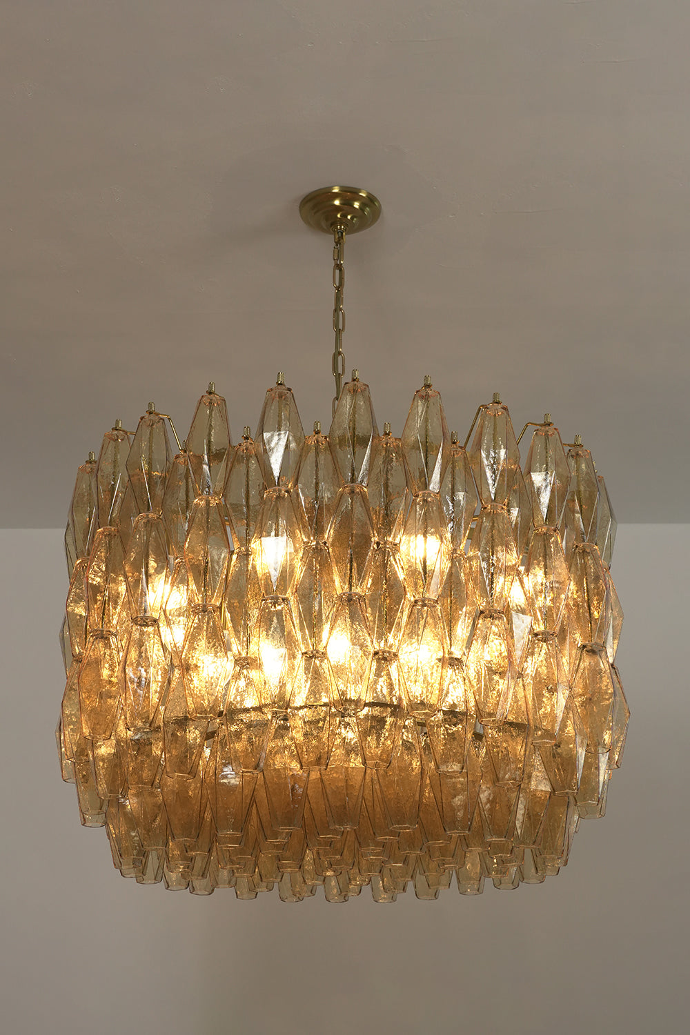 Lit faceted amber glass chandelier | Metal, Glass | Side view against a dark background showing warm glow | Samu Lamp