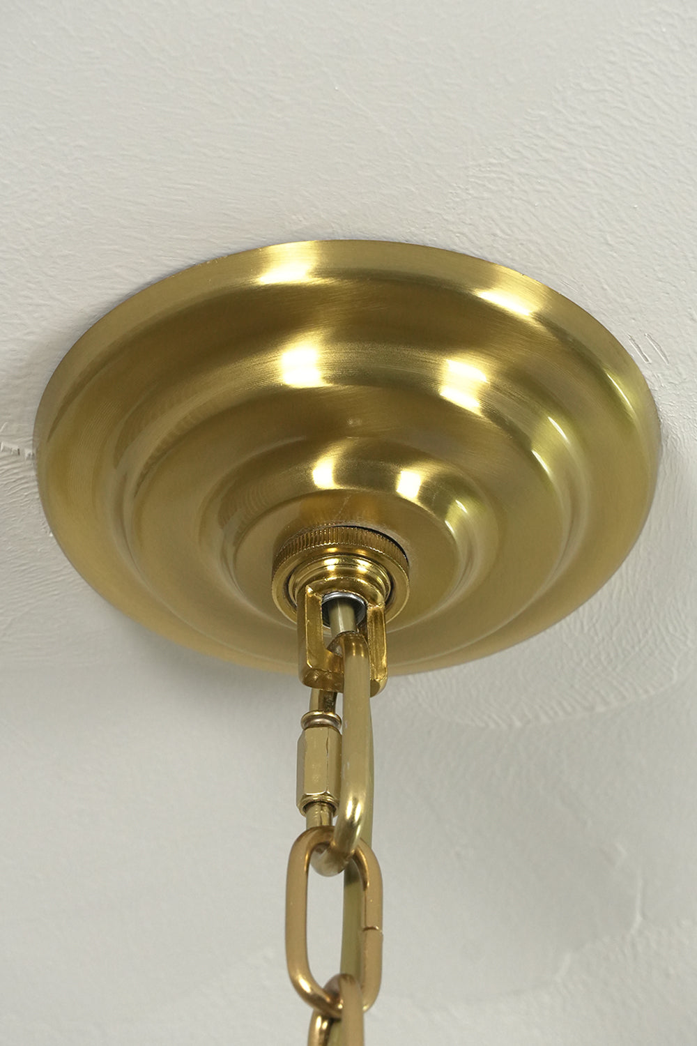 Brass finish ceiling canopy and chain connection | Metal | Close-up of the mounting hardware for chandelier | Samu Lamp