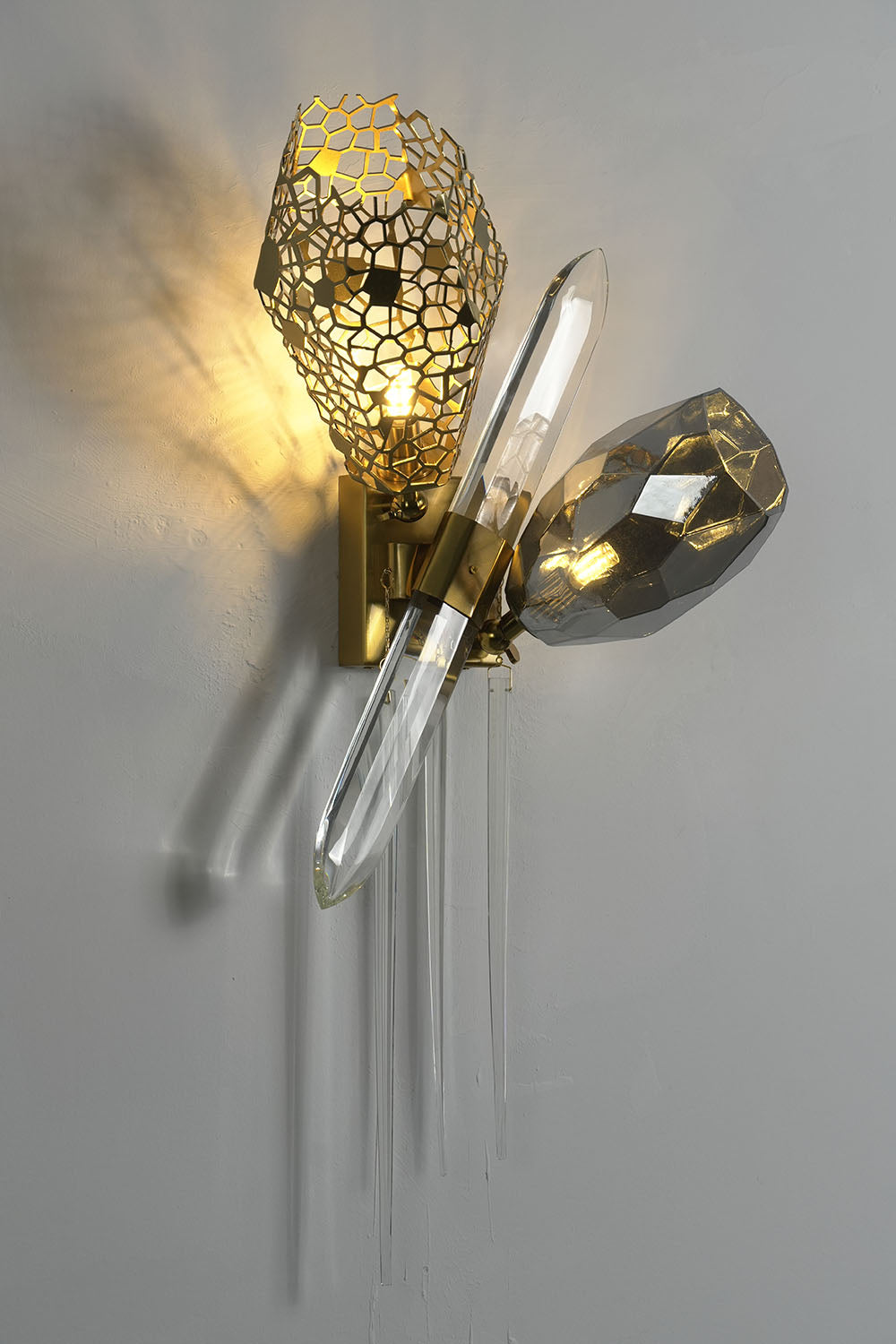 Faucenne Pierced Shade Crystal Spear Wall Lamp | Cut Crystal and Brass | Full product view illuminated gracefully on a grey wall | Samu Lamp