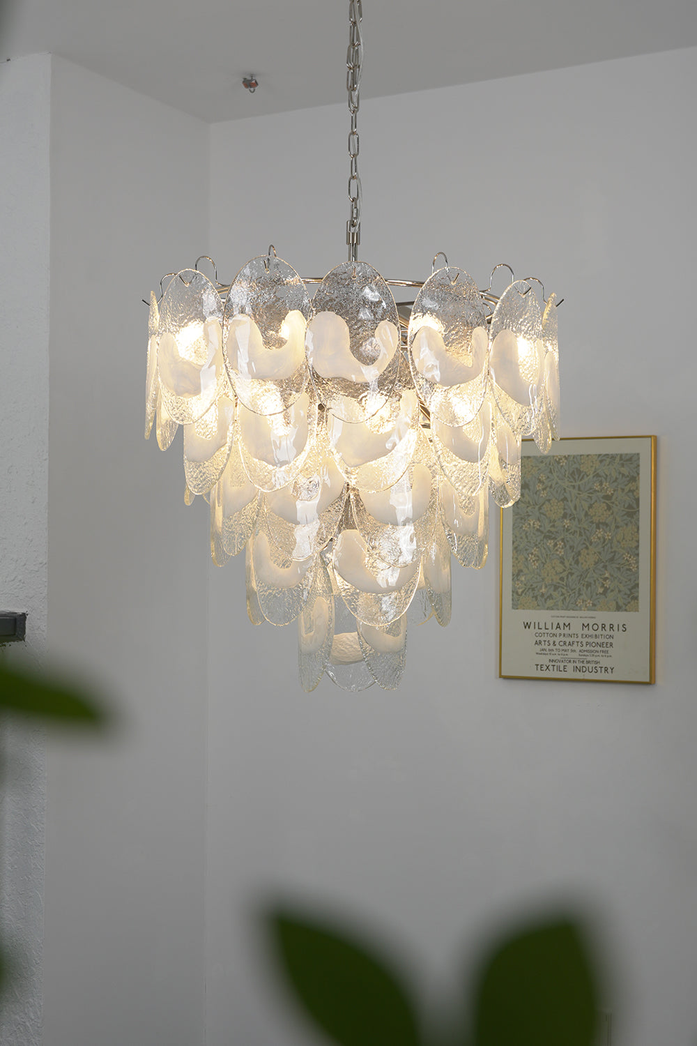 Lit Frostelle Art Chandelier against a white wall | Metal, Glass | Close-up view showing the warm glowing leaves | Samu Lamp