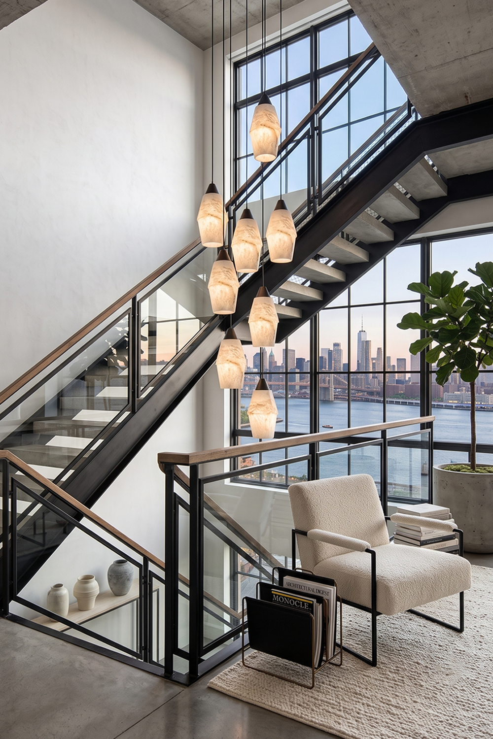 Gemma Staggered Alabaster Cluster Chandelier | Staircase Foyer Light | Suspended in a tall double-height entryway casting a warm golden glow over a modern lounge armchair | Samu Lamp