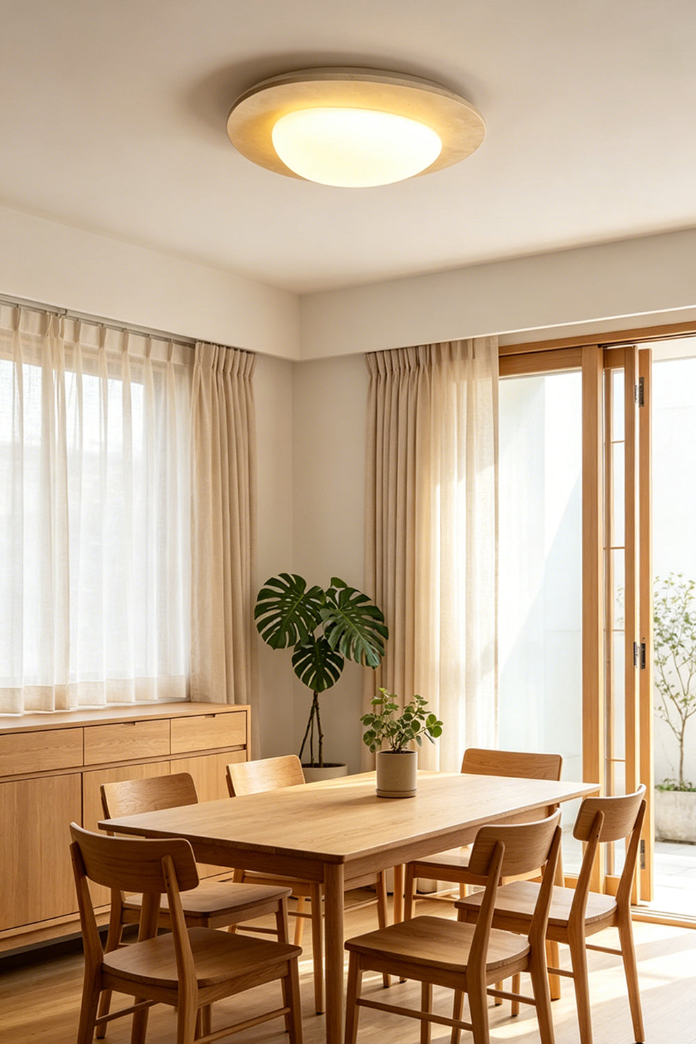 Geoidal Halo Travertine Ceiling Light | Travertine, Glass | Lit over a wooden dining table with chairs and potted plants | Samu Lamp
