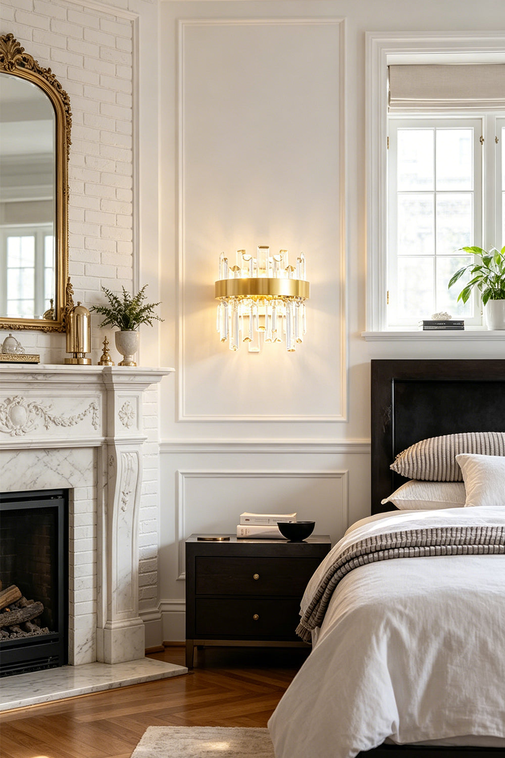 Glacia Tiered Crystal Statement Wall Lamp | Crystal, Metal | Installed on a white wall over a dark wood nightstand next to a classical fireplace mantle with a gold mirror in a refined bedroom suite | Samu Lamp