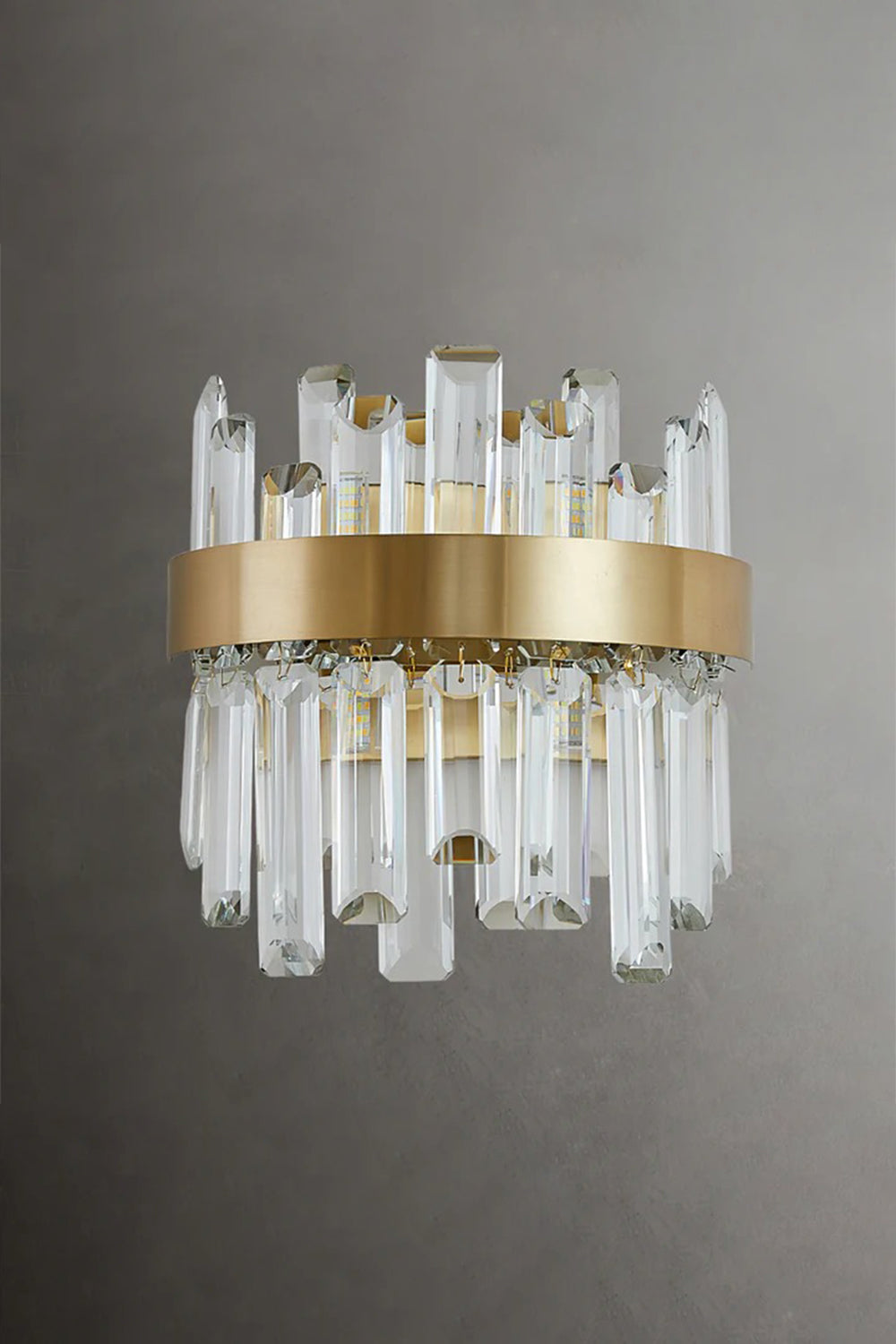 Glacia Tiered Crystal Statement Wall Lamp | Crystal, Metal | Unlit studio view of the modern crystal wall lamp showcasing the glass clarity and gold metal hardware against a dark grey background | Samu Lamp