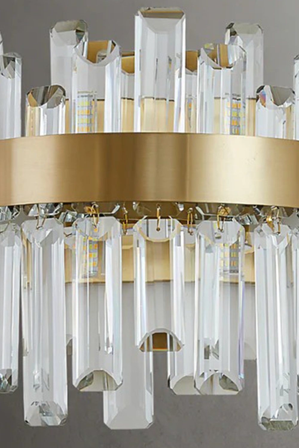 Glacia Tiered Crystal Statement Wall Lamp | Crystal, Metal | Detailed shot of the brushed satin finish on the gold metal band securing the two layers of transparent geometric crystal pillars | Detail shot | Samu Lamp