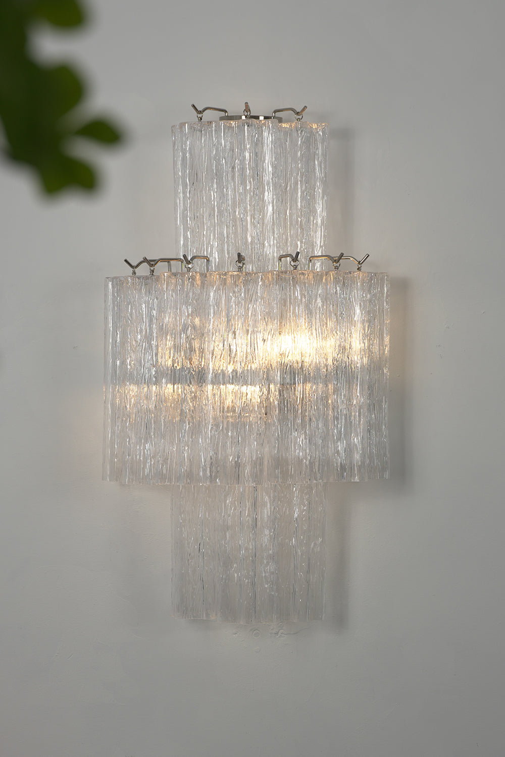 Lit glacier glass wall light showcasing ice texture | Metal, Glass | Close-up view against a grey wall | Samu Lamp