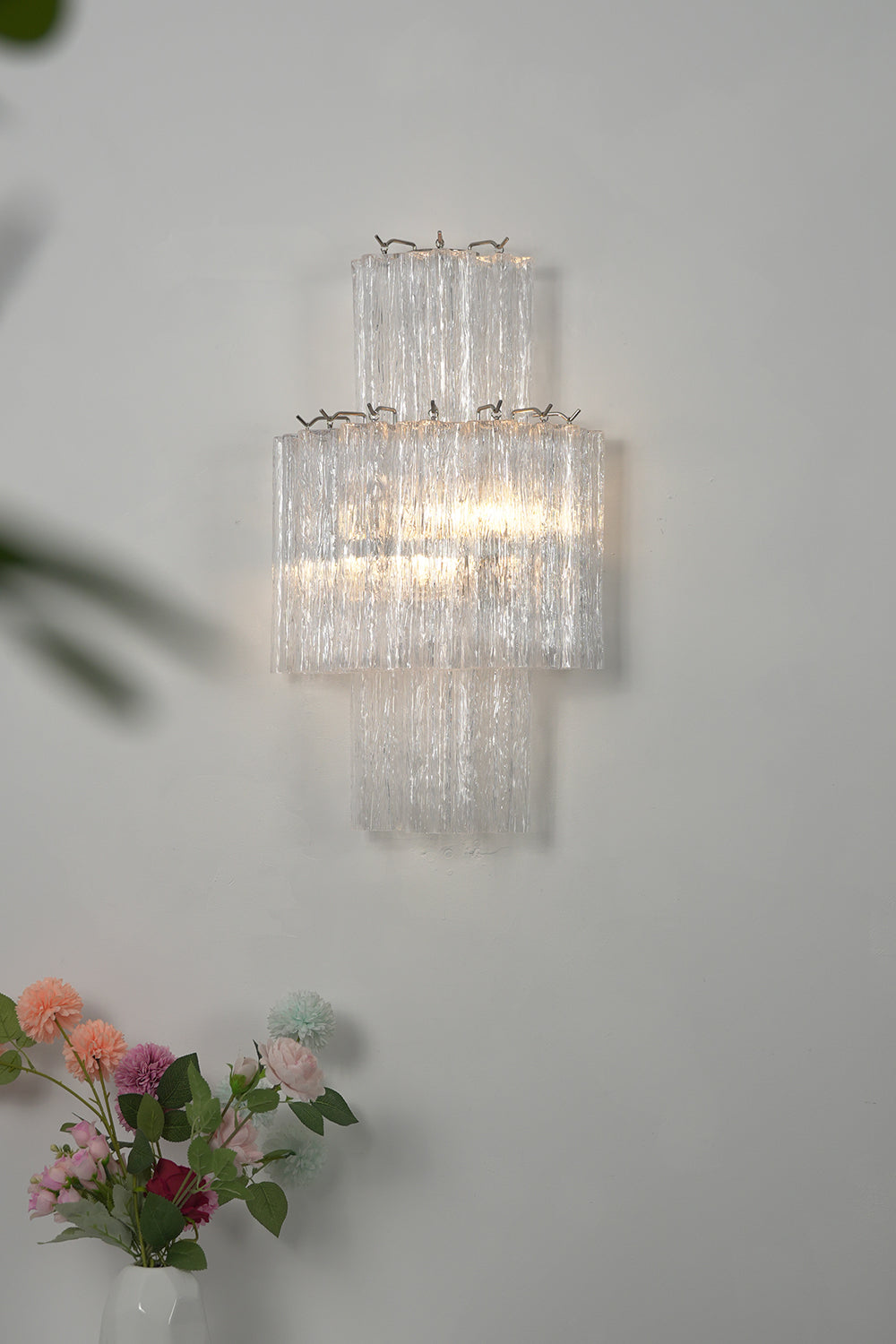 Lit glacier modern tiered wall sconce over flowers | Metal, Glass | Studio shot on grey background | Samu Lamp