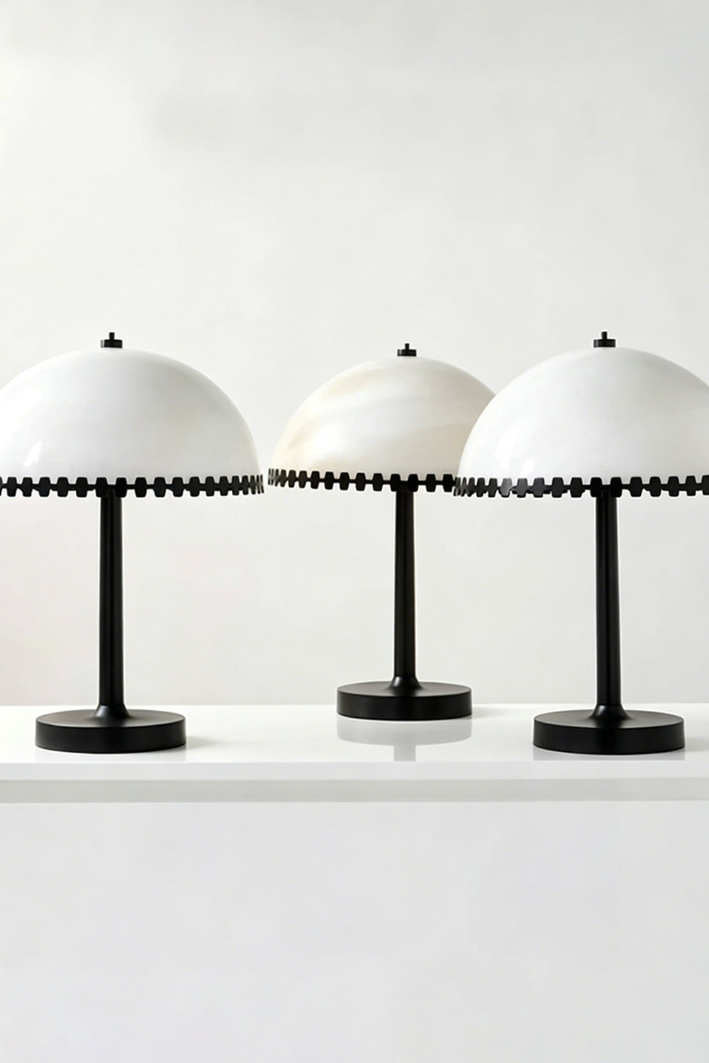 Helena Alabaster Trim Table Lamp | Product Group Shot | A collection of three identical minimalist dome-shaped stone table lamps lined up neatly on a clean white display shelf | Samu Lamp