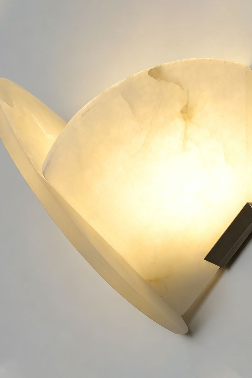 Hollis Angled Alabaster Wall Lamp | Natural Alabaster and Metal | Side close-up view showing warm light reflection against a wall | Samu Lamp