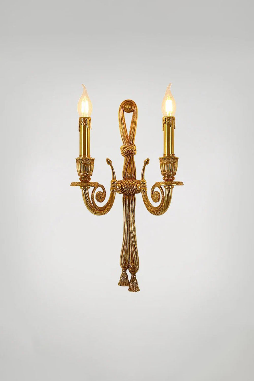 Honoria Rope and Tassel Brass Sconce | Brass and Metal | Studio shot showing the full sconce glowing warmly against a grey backdrop | Samu Lamp