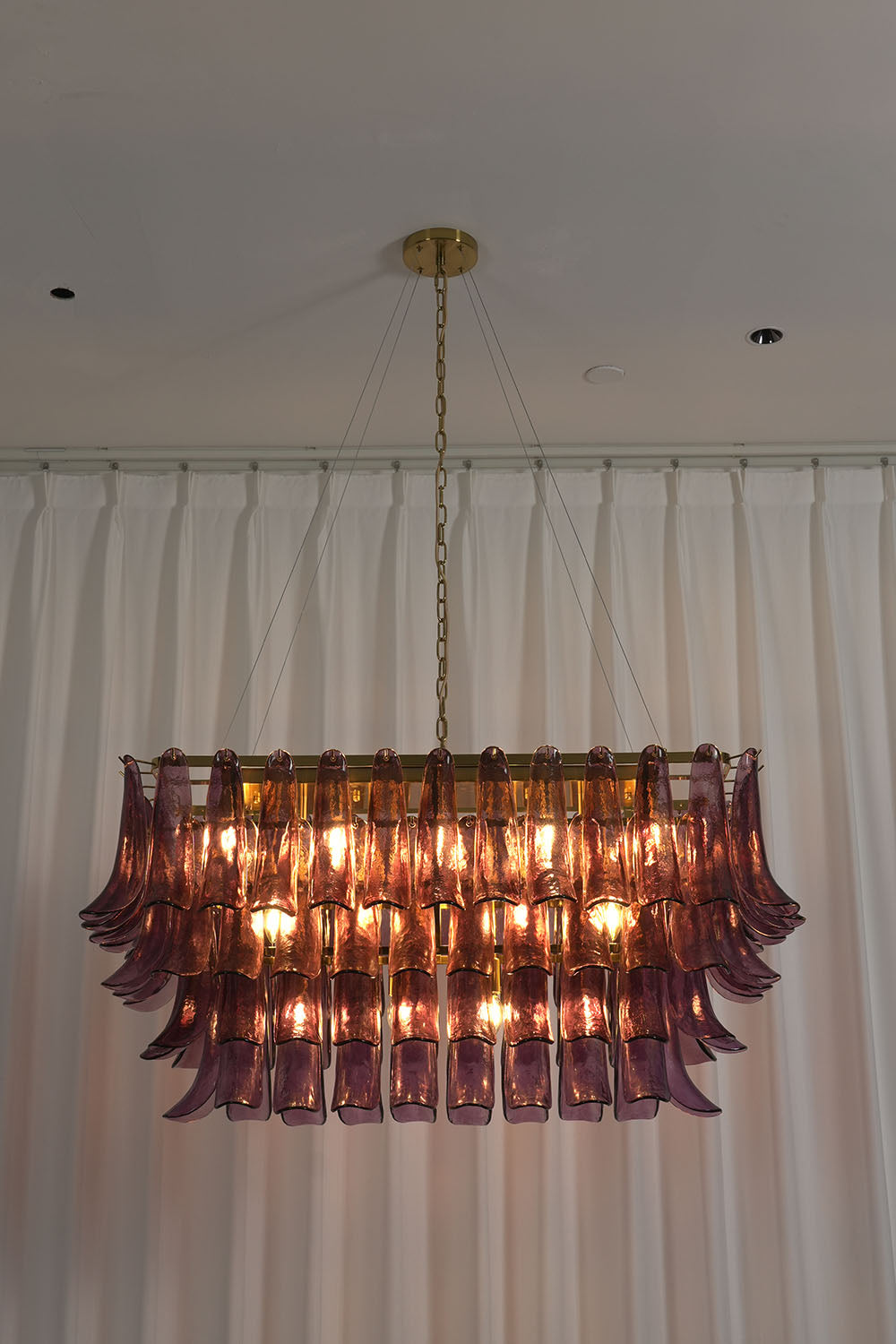 Ilvesse Amethyst Glass Petal Rectangular Chandelier | Amethyst Glass and Brass | Real-life view illuminated displayed on a neutral wall backdrop | Samu Lamp