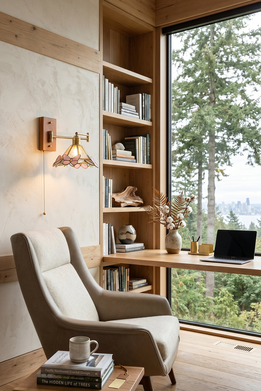 Iris Butterfly Stained Glass Wall Lamp | Stained Glass, Metal, Wood | Providing warm task light over a comfortable grey upholstered armchair and built-in wooden bookshelves facing a scenic forest window | Samu Lamp
