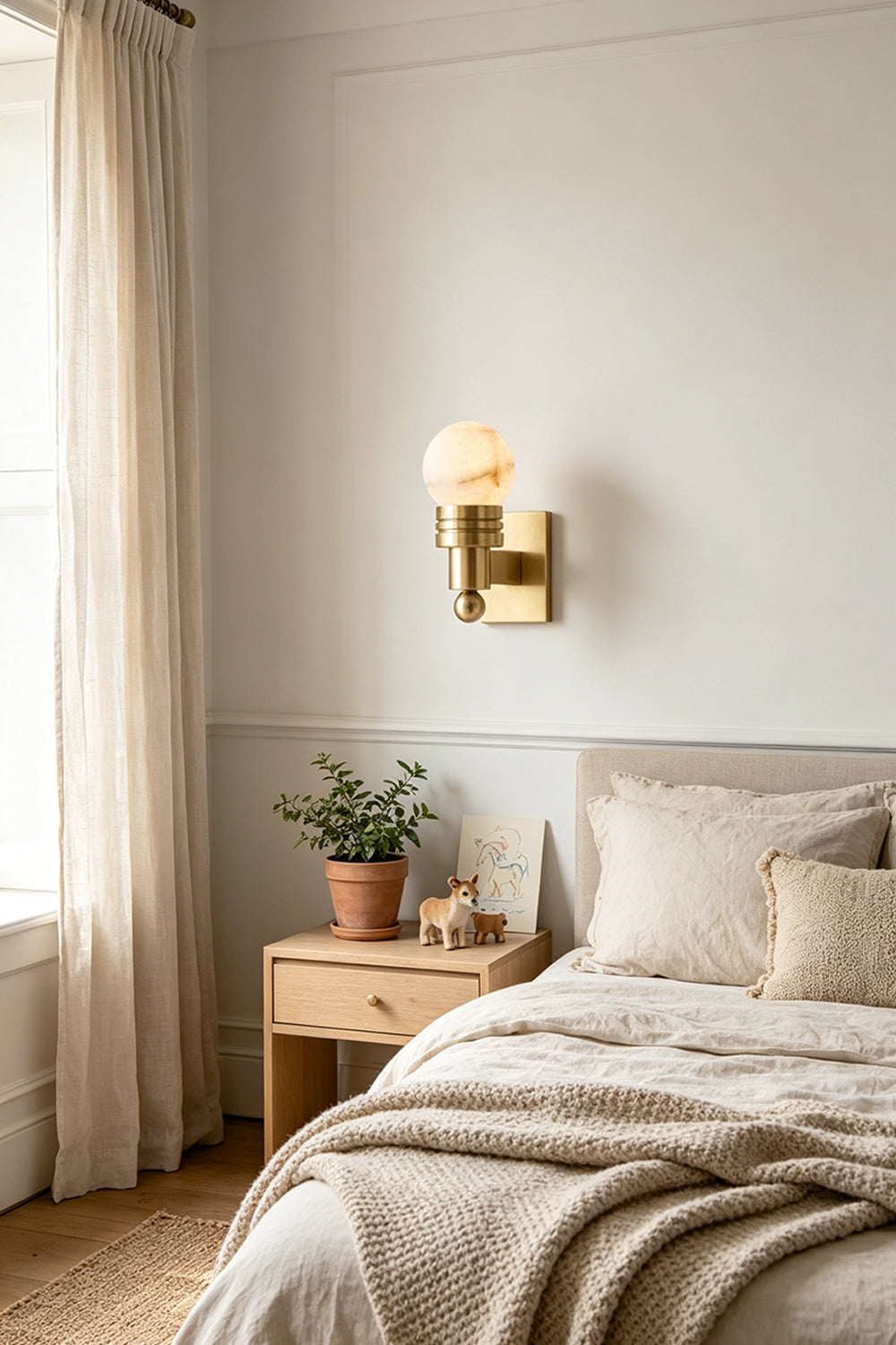 Isolde Alabaster Orb Wall Sconce | Natural Alabaster and Aged Brass | Installed as a bedtime reading light beside a cozy neatly made bed in a bedroom | Samu Lamp