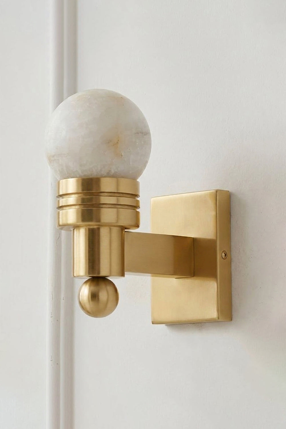 Isolde Alabaster Orb Wall Sconce | Natural Alabaster and Aged Brass | Full view of the elegant single wall lamp mounted on a clean light beige wall | Samu Lamp