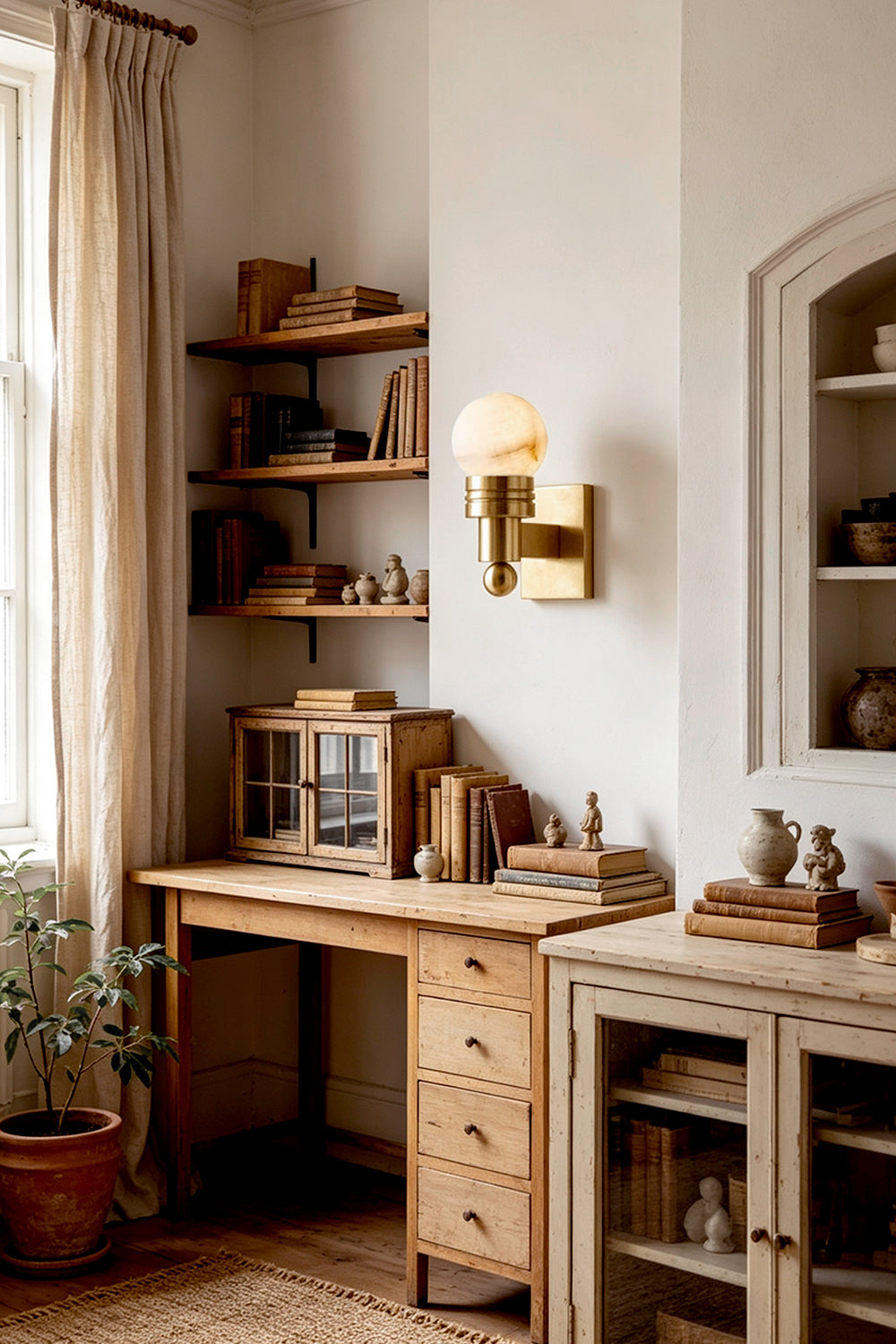 Isolde Alabaster Orb Wall Sconce | Natural Alabaster and Aged Brass | Mounted on a wall above a vintage wooden study desk and shelves in a warm room | Samu Lamp
