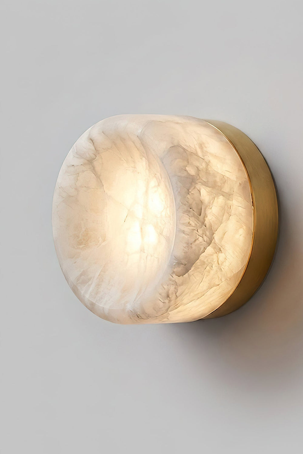 Isolde Concave Alabaster Disc Wall Sconce | Natural Alabaster and Black Metal | Studio close-up shot of the lit sconce featuring a matte black finish base on a light wall | Samu Lamp