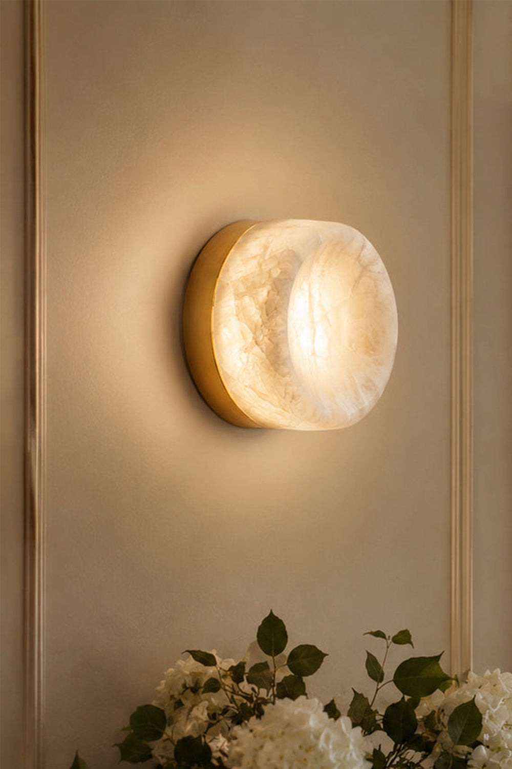 Isolde Concave Alabaster Disc Wall Sconce | Natural Alabaster and Brass | Close-up of the fixture glowing on a beige wall creating a beautiful light halo | Samu Lamp