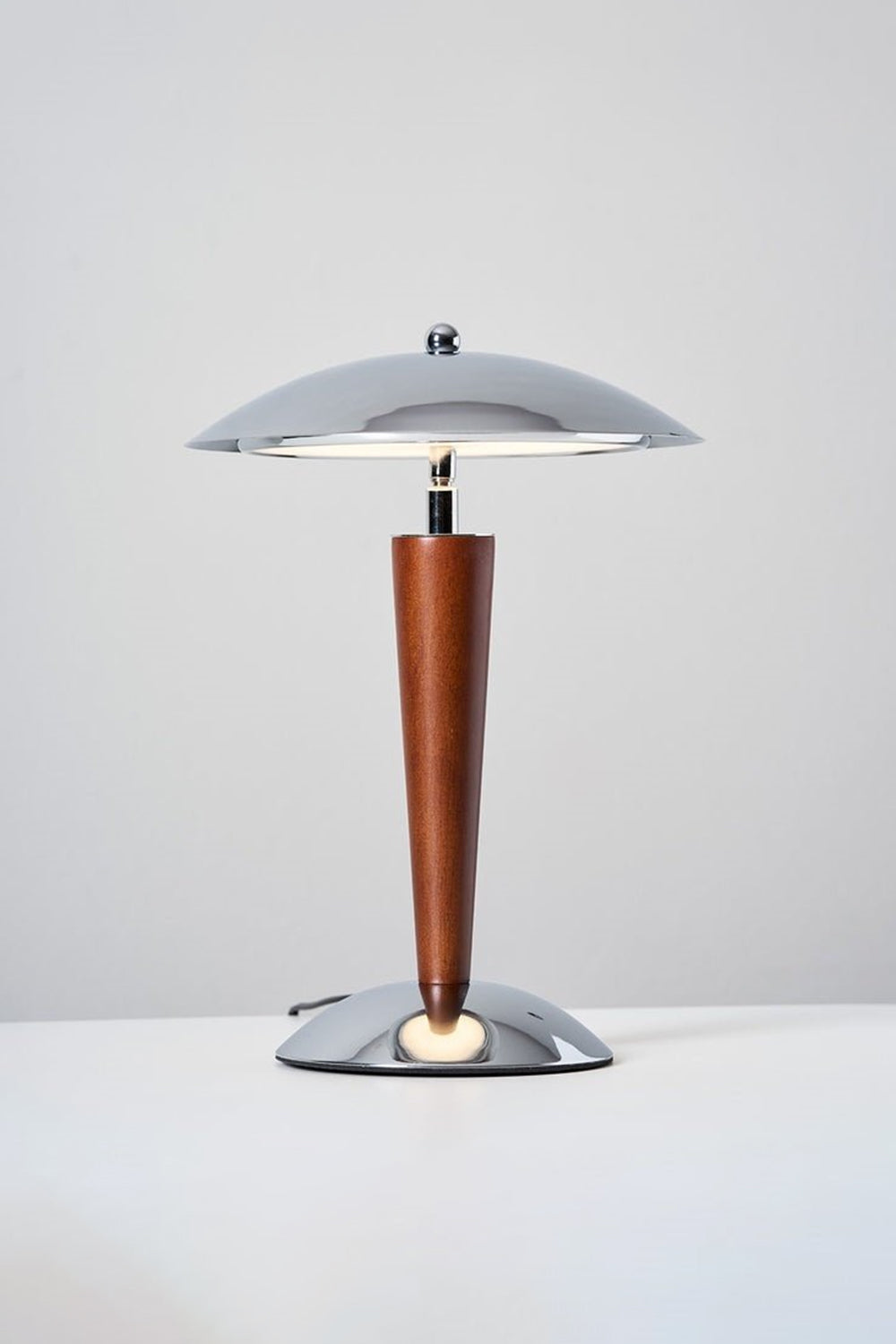 Isolde Domed Walnut Table Lamp | Illuminated Neck Detail | Close-up view underneath the lit dome shade showcasing the reflection on the chrome hardware and the top wood finish | Detail shot | Samu Lamp