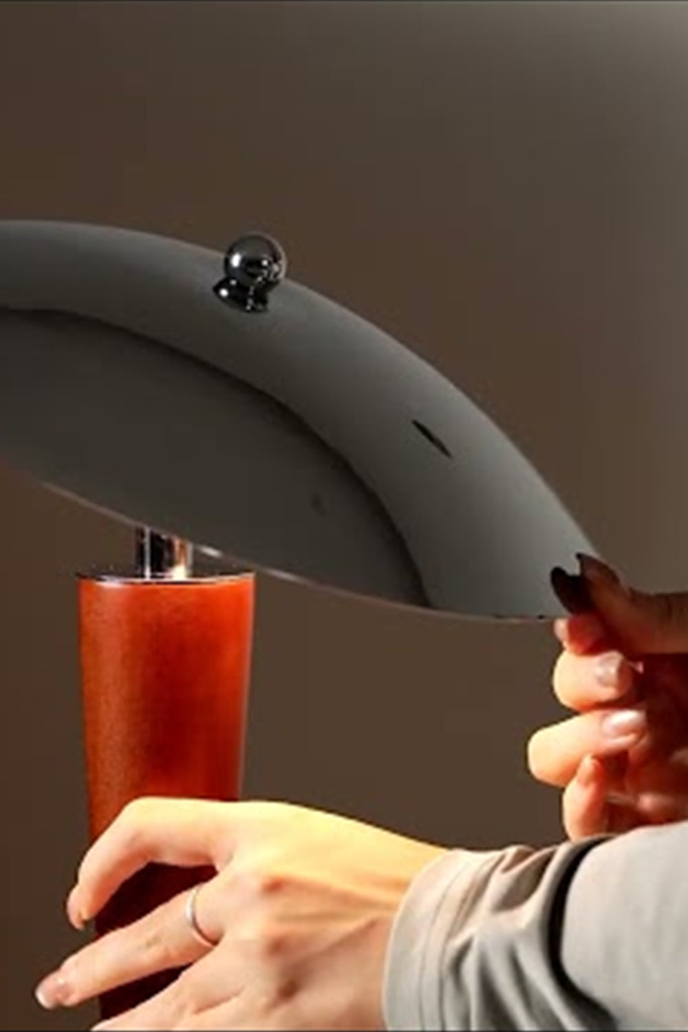 Isolde Domed Walnut Table Lamp | Adjusting Shade Detail | Detailed close-up shot showing a person's hand adjusting the sleek polished chrome dome shade of the lit table fixture | Detail shot | Samu Lamp