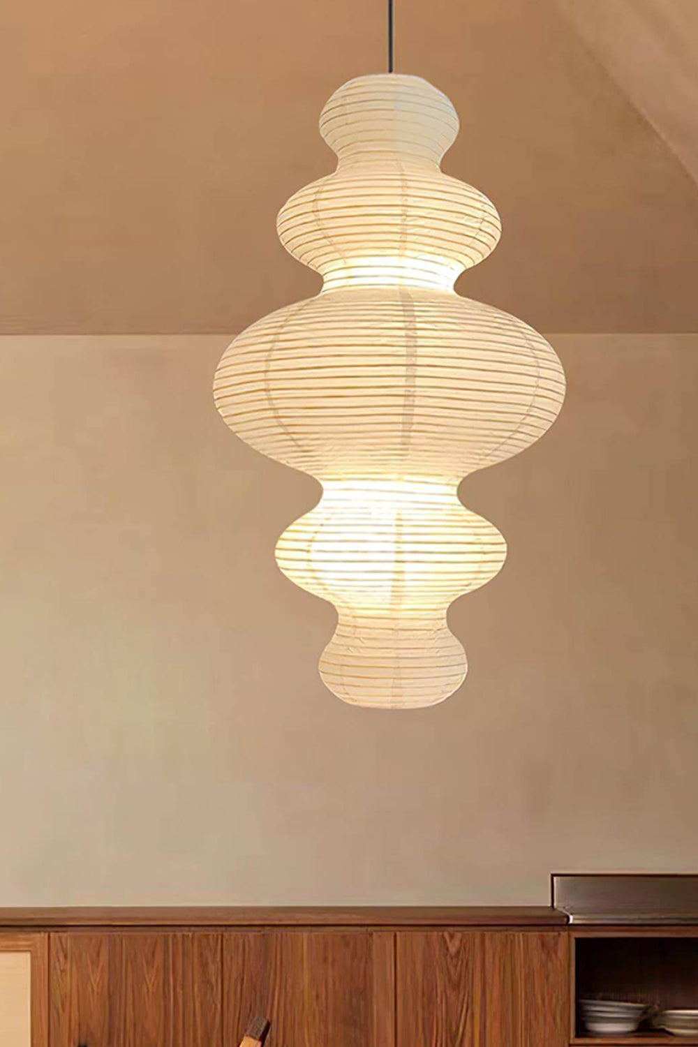 Isolde Stacked Paper Pendant Lamp | Textured Ribbed Paper | Suspended above a classic dark wood storage cabinet against a minimalist beige wall | Samu Lamp