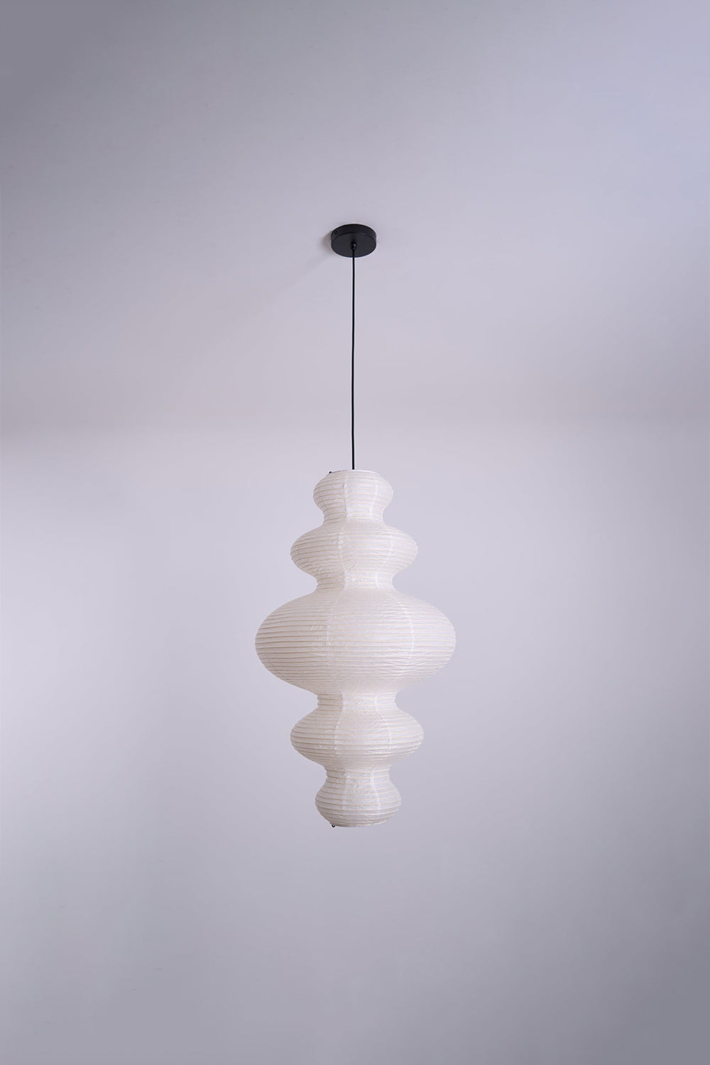 Isolde Stacked Paper Pendant Lamp | Textured Ribbed Paper | Full view of the sculptural light fixture hanging from a plain ceiling against a light wall | Samu Lamp