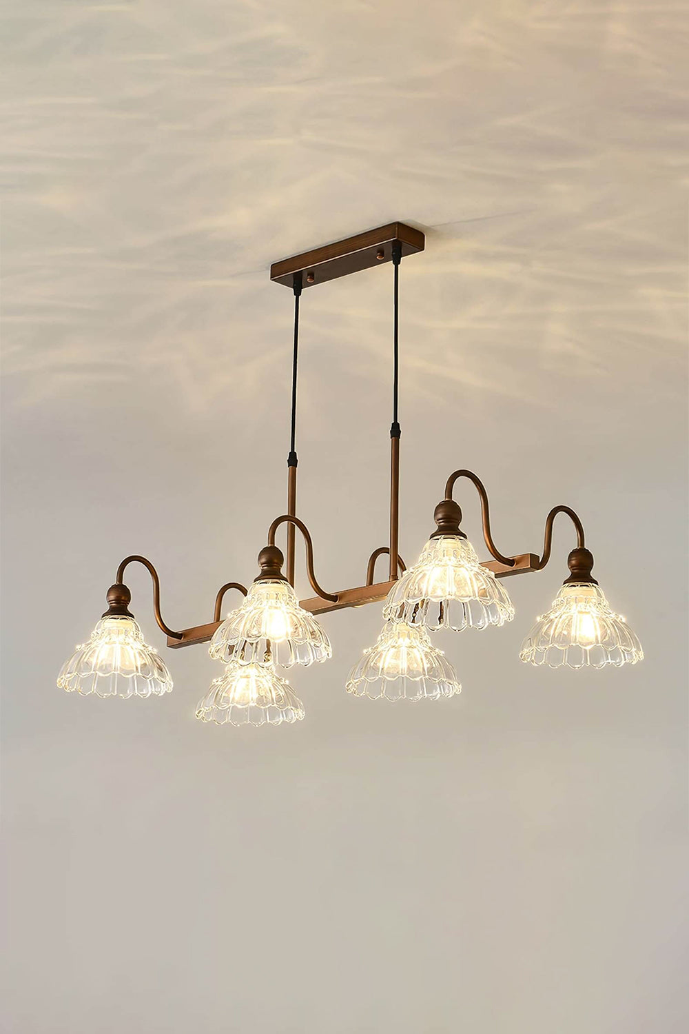 Isolde Vintage Glass Long Chandelier | Warm Halo Effect | Staged studio shot of the illuminated linear glass chandelier projecting a beautiful golden light pattern onto a warm cream ceiling | Samu Lamp
