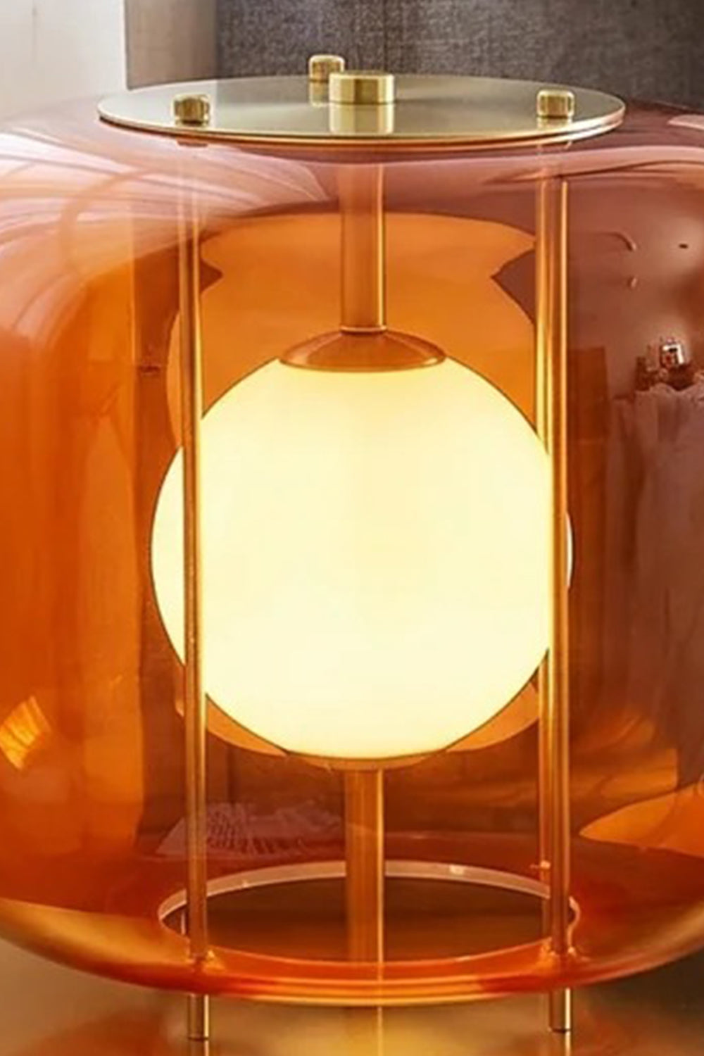 Jasper Colorblock Table Lamp | Glass, Metal | Macro close-up focus on the illuminated orange glass variant showing the top brass plate, structural wires, and frosted white light bulb globe | Detail shot | Samu Lamp