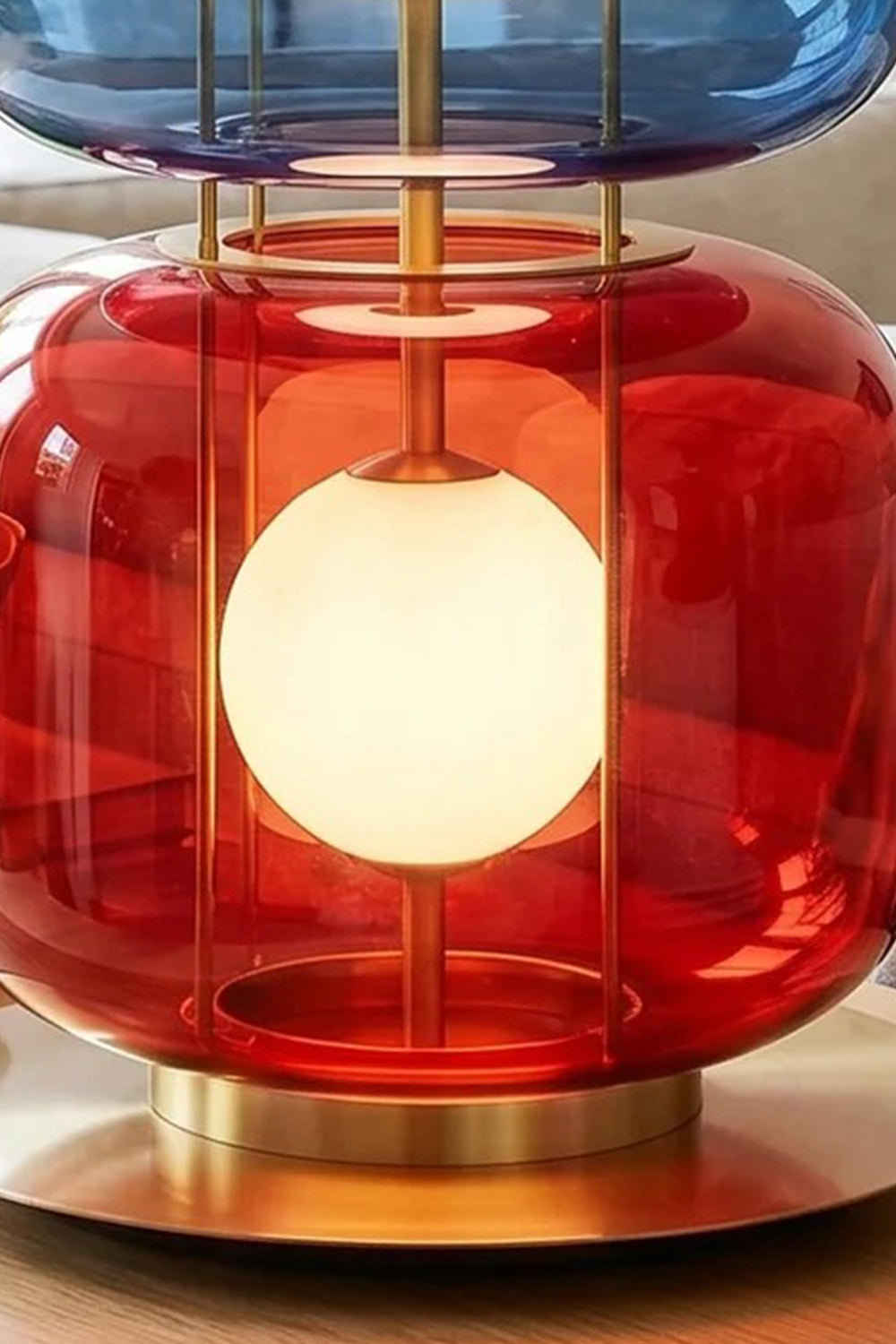 Jasper Colorblock Table Lamp | Glass, Metal | Detailed close-up view focusing on the glowing red translucent glass lower block and the circular brushed gold brass base plate | Detail shot | Samu Lamp