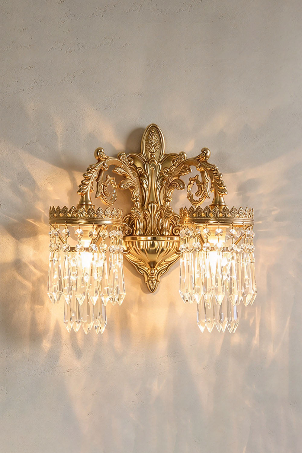 Josseline Brass Crystal Crown Wall Lamp | Cut Crystal and Brass | Front view of the illuminated double-arm sconce casting warm light on a wall | Samu Lamp