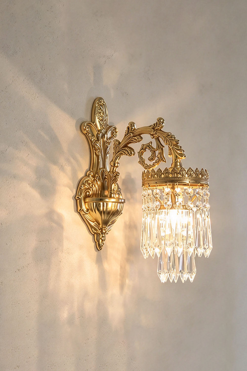 Josseline Brass Crystal Crown Wall Lamp | Cut Crystal and Brass | Side view of the illuminated single-arm crystal sconce on a neutral wall | Samu Lamp