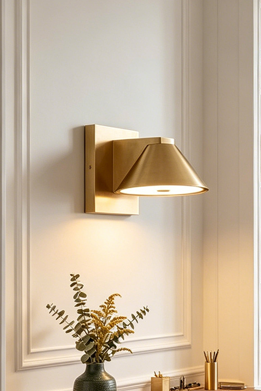 Kaelen Brass Cone Wall Sconce | Staged Accent Shot | Side angle staged view of the illuminated brass sconce casting a clear downward pool of warm light on a classic white wall | Samu Lamp