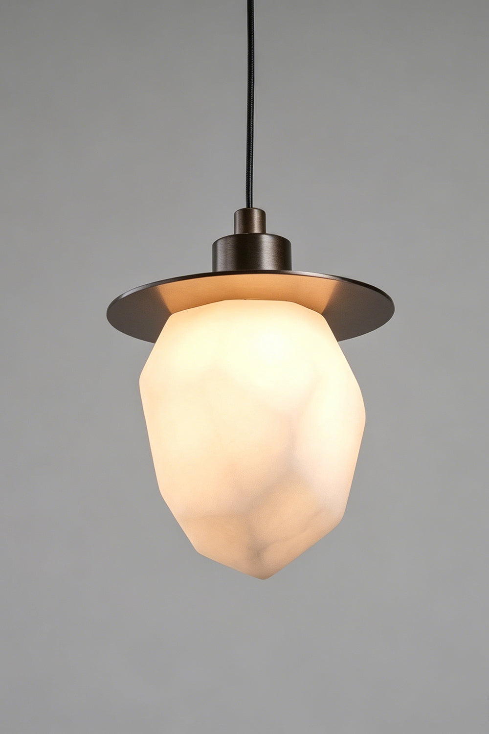 Kaelen Faceted Alabaster Pendant Light | Alabaster, Metal | Studio front view of the fully illuminated faceted stone pendant casting a warm golden light against a grey backdrop | Samu Lamp
