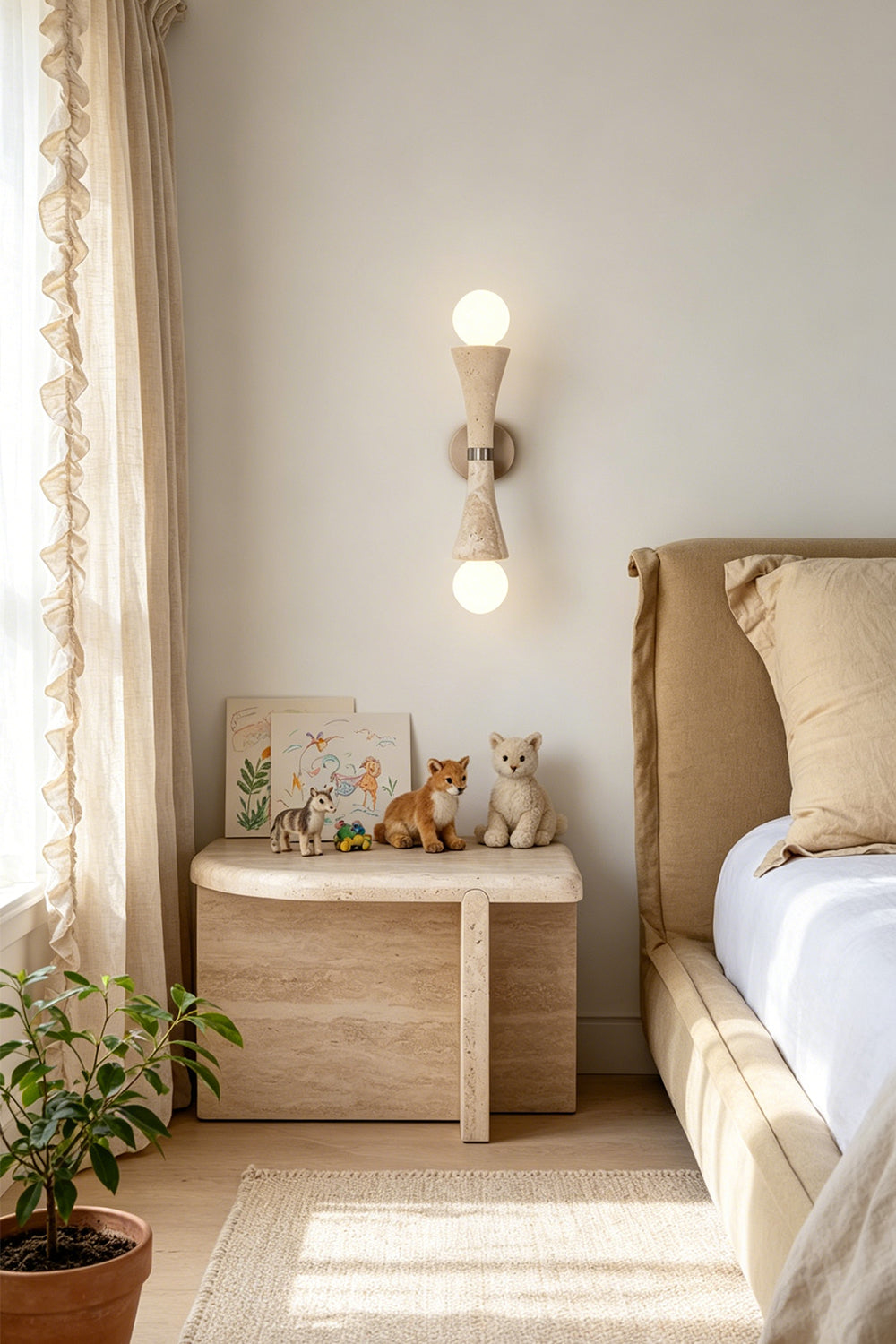 Katia Travertine Hourglass Wall Lamp | Travertine, Metal | Mounted as an elegant bedside reading sconce casting an upward and downward warm glow next to a wooden nightstand and a cozy platform bed | Samu Lamp