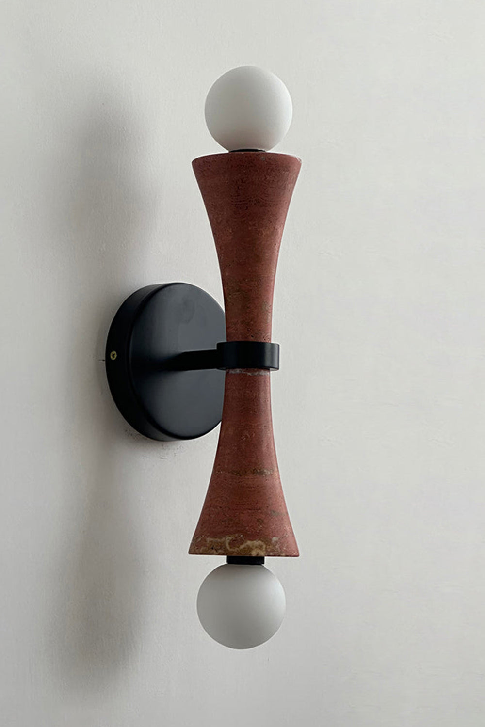 Katia Travertine Hourglass Wall Lamp | Travertine, Metal | Studio variant product view featuring a rich reddish-brown terracotta colored stone hourglass body paired with black hardware | Samu Lamp