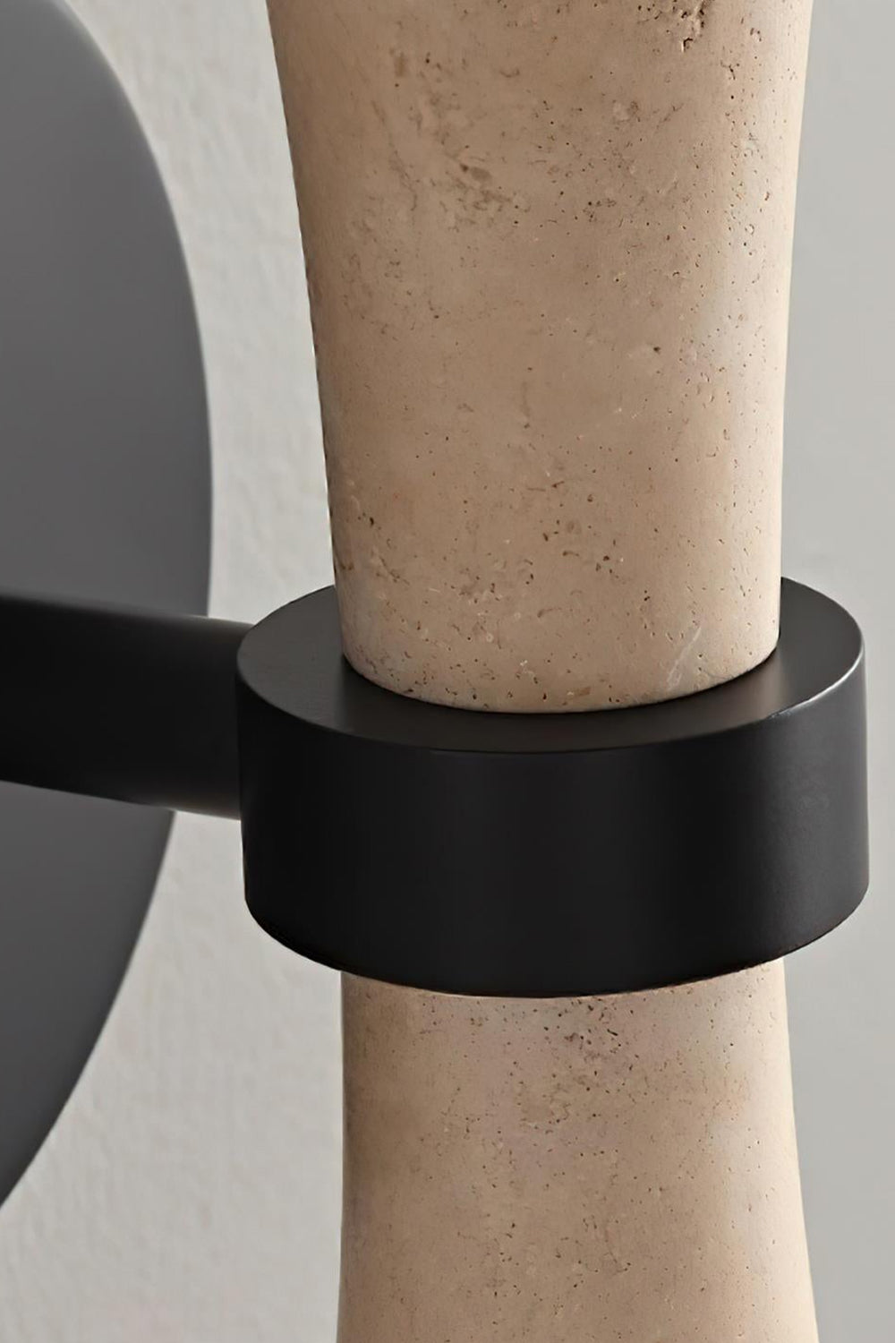 Katia Travertine Hourglass Wall Lamp | Travertine, Metal | Macro close-up focusing on the seamless connection of the matte black metallic wall base mount and holding ring structure | Detail shot | Samu Lamp