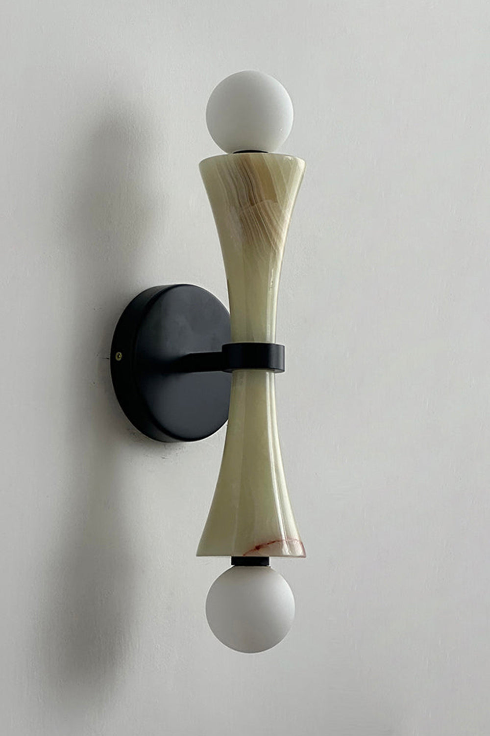 Katia Travertine Hourglass Wall Lamp | Travertine, Metal | Studio variant product view featuring an olive green tinted stone hourglass body paired with matte black hardware fittings | Samu Lamp