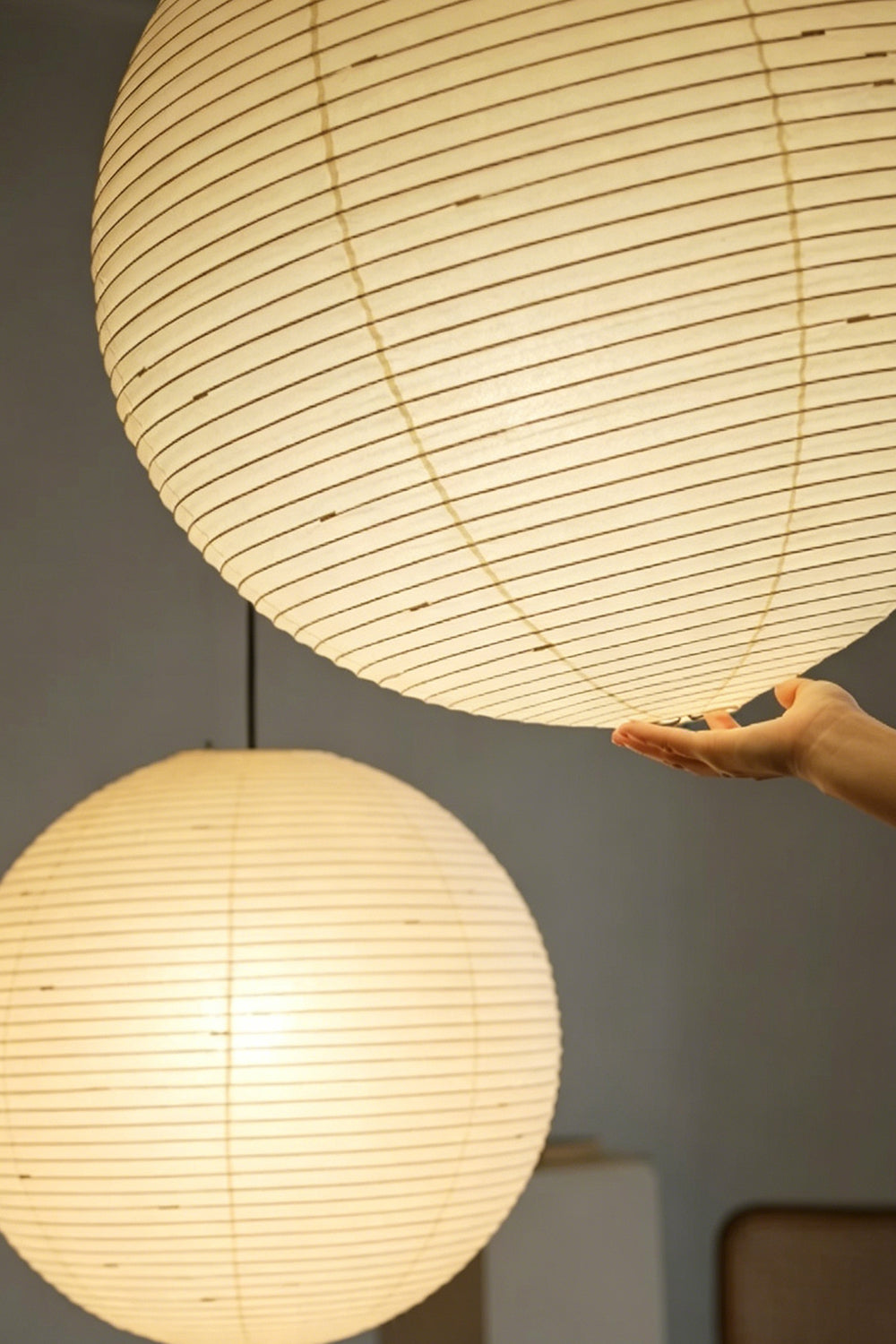 Komorebi Mulberry Paper Pendant Light | Paper, Bamboo | A hand gently touching a fully lit spherical paper lantern shade to demonstrate its soft texture and warm glow | Detail shot | Samu Lamp