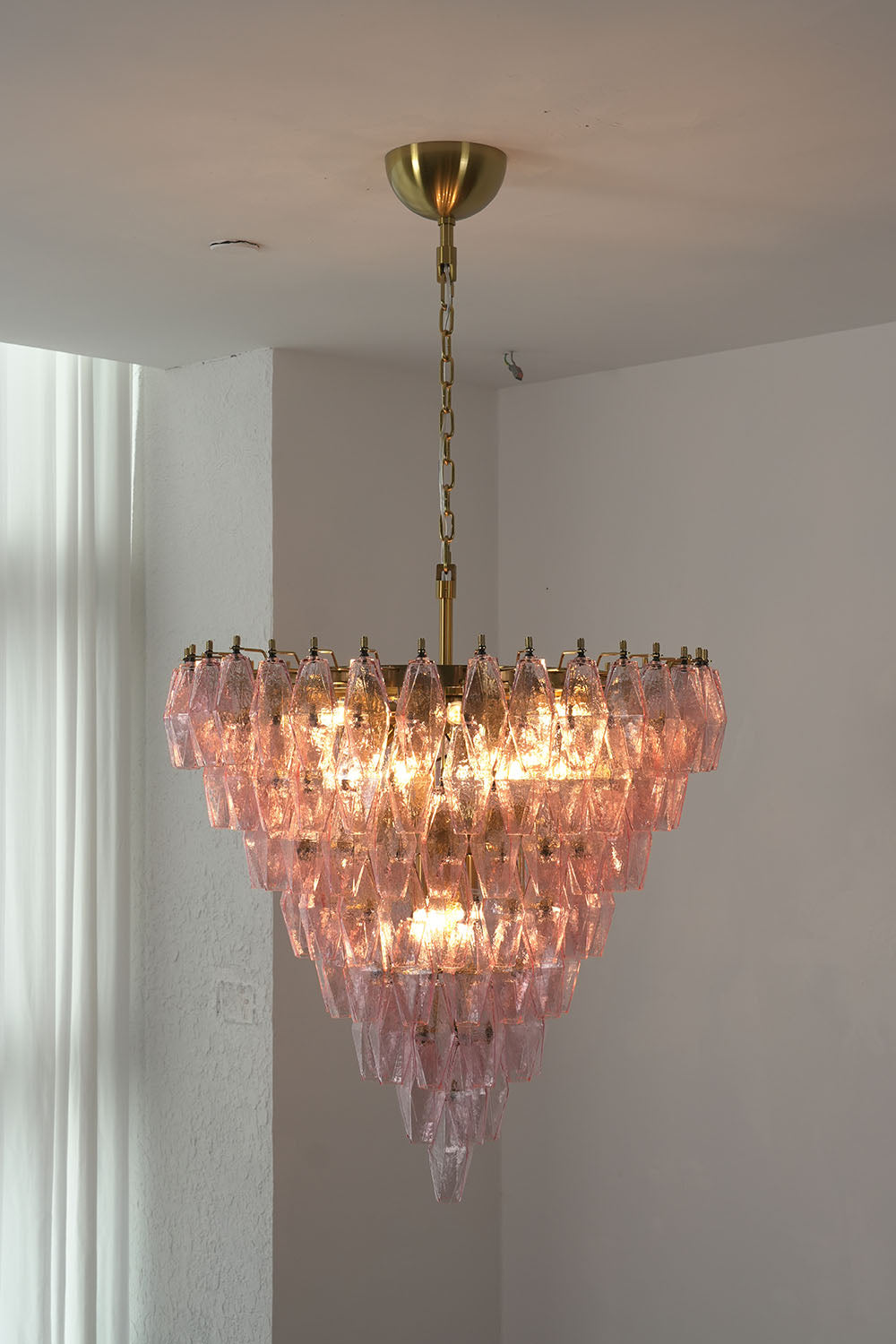 Lauragne Pink Faceted Glass Cascade Chandelier | Pink Faceted Glass and Brass | Real-life installation view glowing softly near a white wall | Samu Lamp