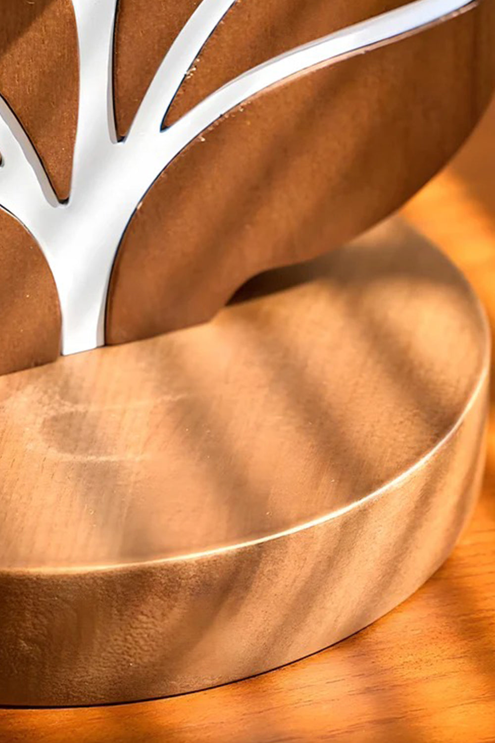 Leafora Botanical Leaf Table Light | Wood, Fabric, Leather | Macro close-up view of the sculpted warm brown wood lamp base showcasing the clean white inlaid botanical leaf vein lines under golden sunlight stripes | Detail shot | Samu Lamp