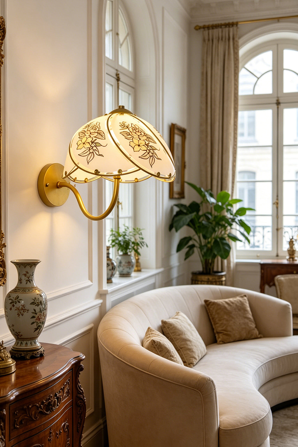 Lillian Retro Floral Wall Lamp | Glass, Metal | Providing a warm ambient glow over a curved cream sofa and antique wooden cabinet near a window | Samu Lamp