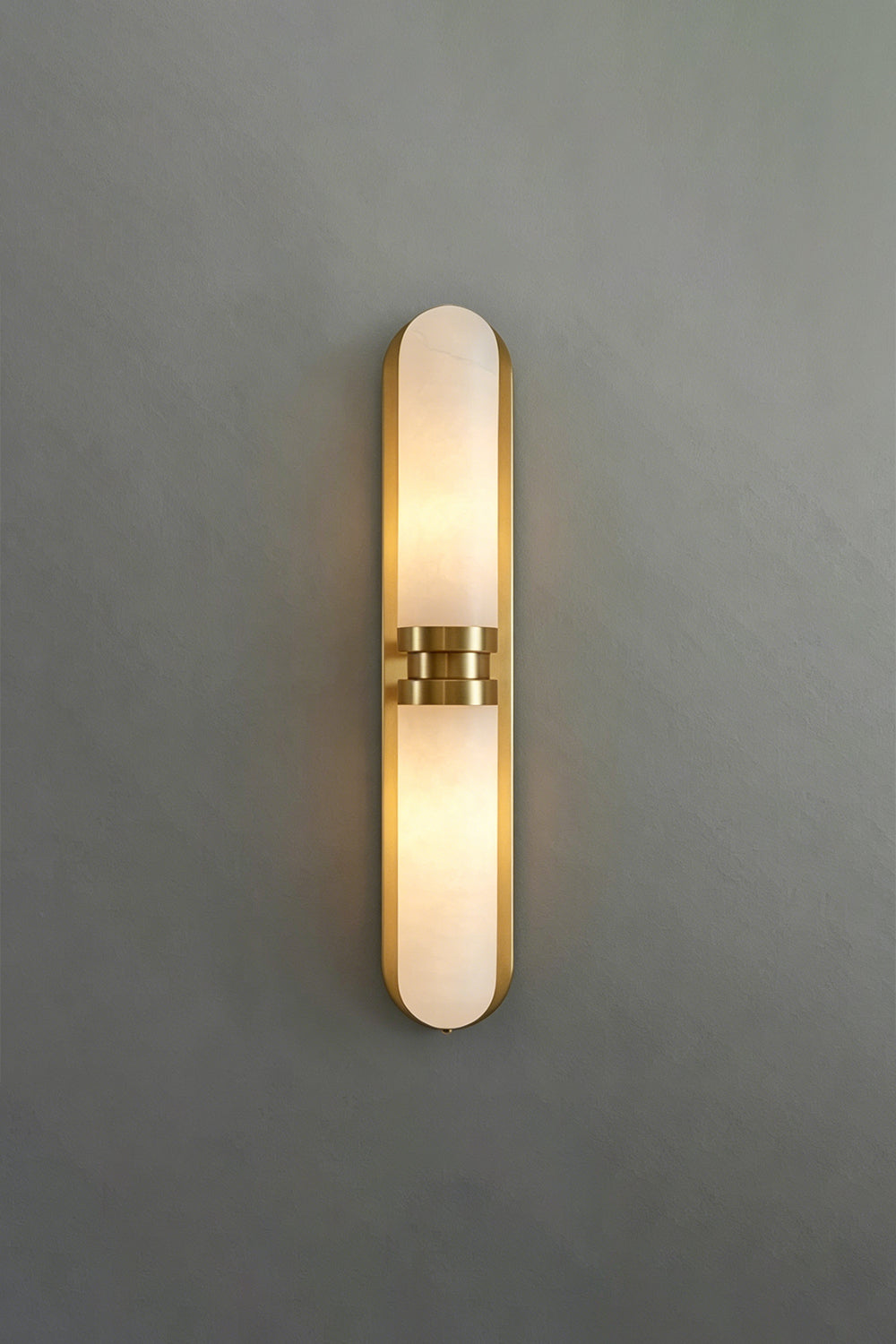 Linea Alabaster Capsule Wall Sconce | Alabaster, Brass | Frontal studio view of the fully lit linear capsule stone sconce casting a warm glow against a minimalist grey background | Samu Lamp