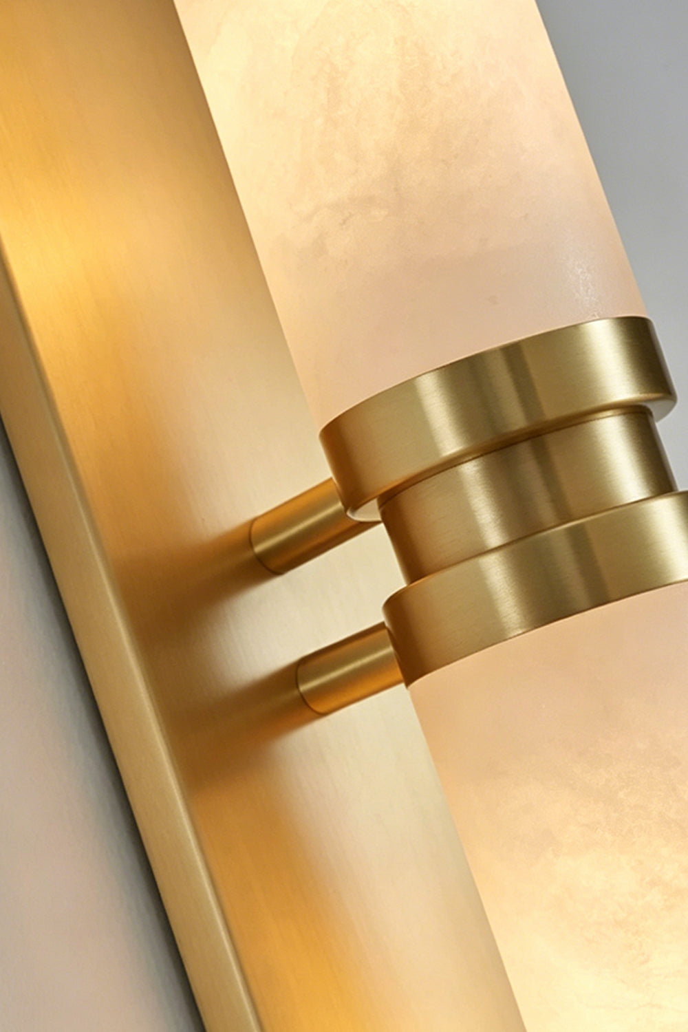 Linea Alabaster Capsule Wall Sconce | Alabaster, Brass | Close-up detail shot highlighting the textured alabaster stone cylinder and the central brushed brass bracket ring fixture | Detail shot | Samu Lamp