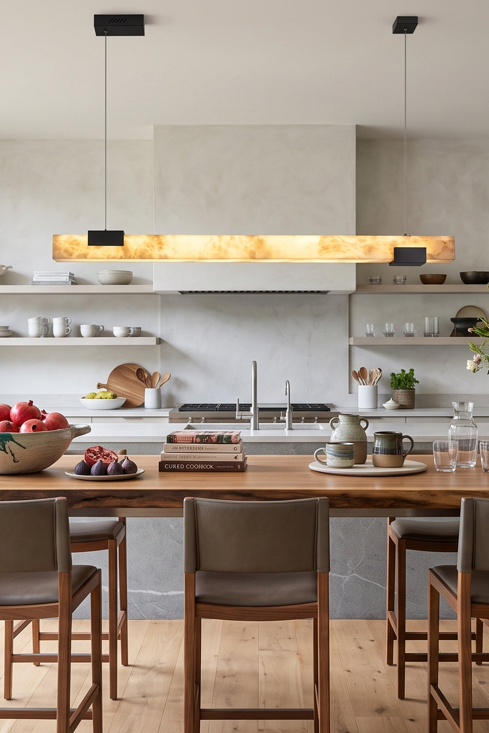 Liora Linear Alabaster Pendant Light | Natural Alabaster and Black Metal | Casting a warm ambient glow over a wooden kitchen counter and elegant high-back bar chairs | Samu Lamp