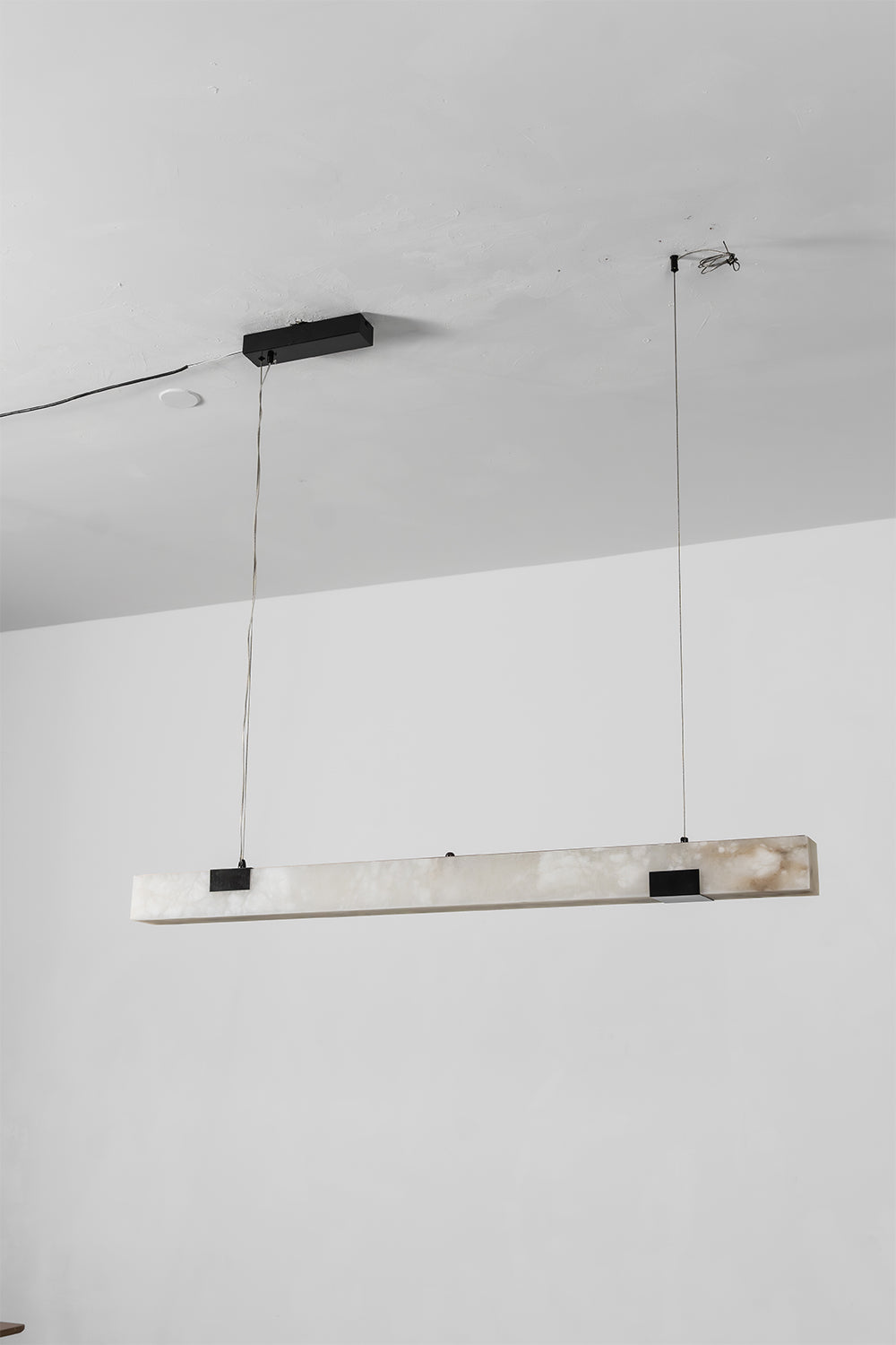 Liora Linear Alabaster Pendant Light | Natural Alabaster and Black Metal | Full studio product view of the unlit long linear fixture hanging from slim ceiling wires | Samu Lamp